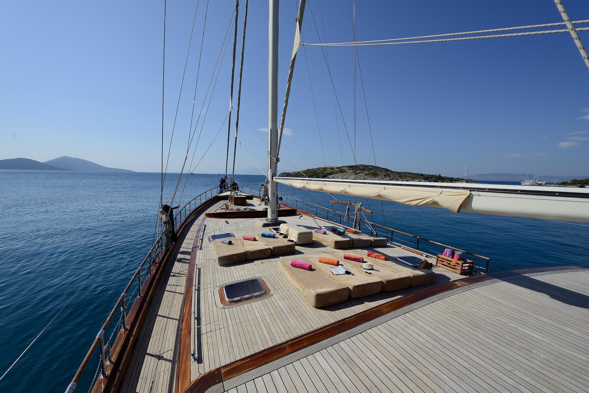 gulet forward deck with cushioned seating area, mast rigging and Mediterranean coastline view