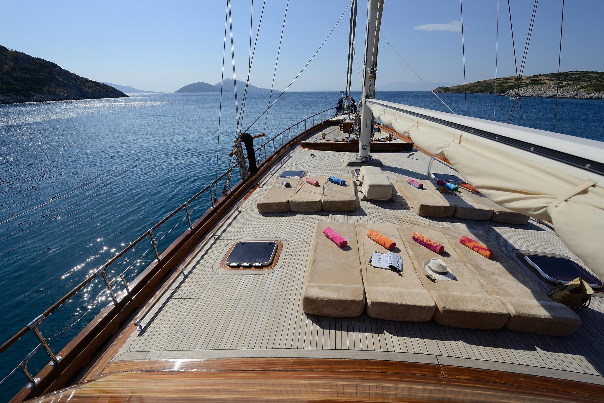 gulet forward deck with beige lounging cushions, teak decking, and white sail covers