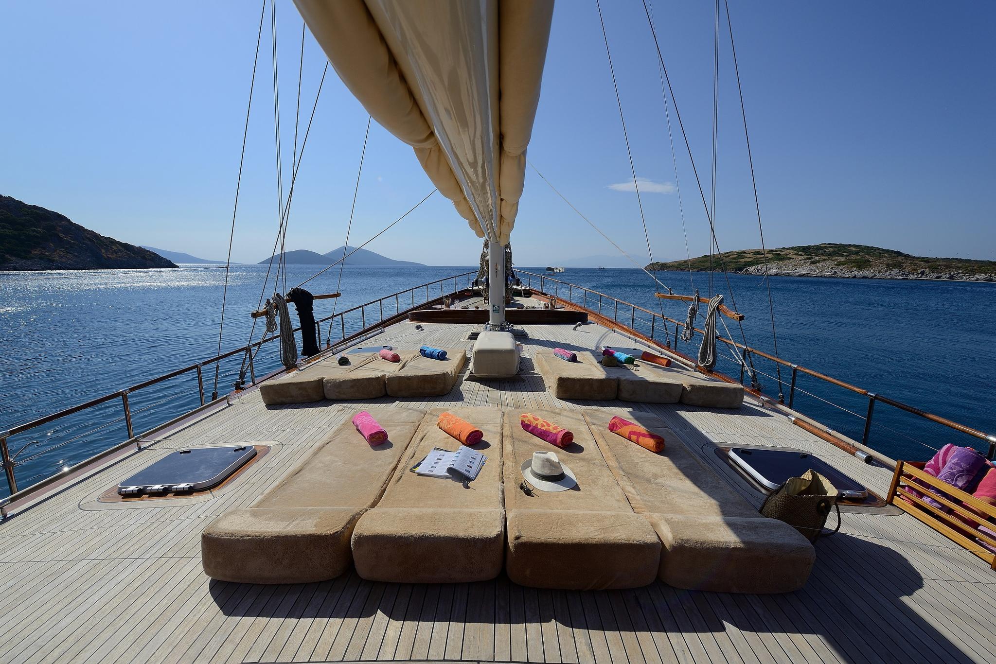 gulet forward deck with raised sail and beige cushions under blue sky
