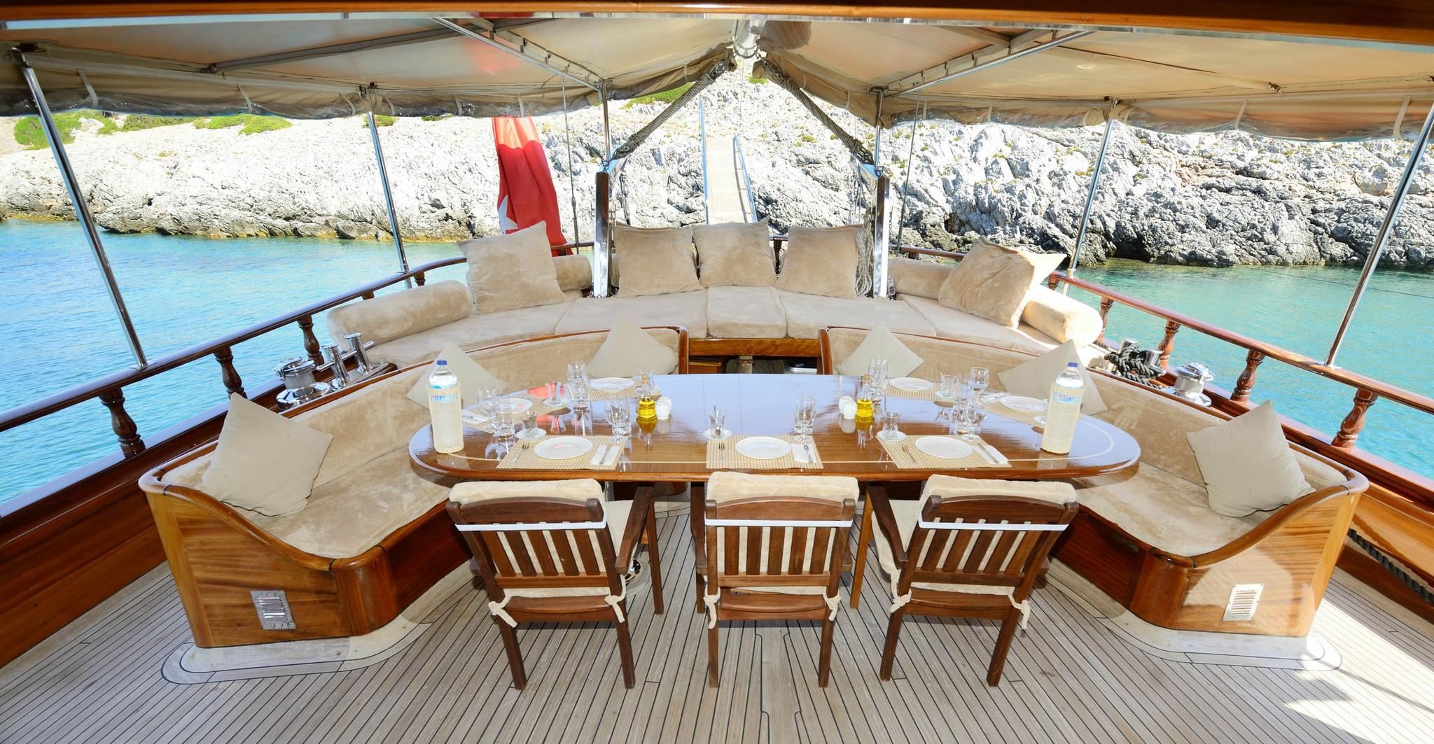 gulet aft deck dining area with U-shaped seating, oval table and coastal backdrop