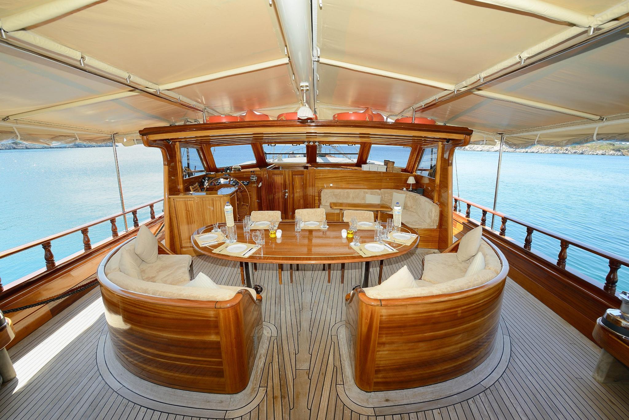 Luxury yacht aft deck with curved wooden banquette seating around oval dining table