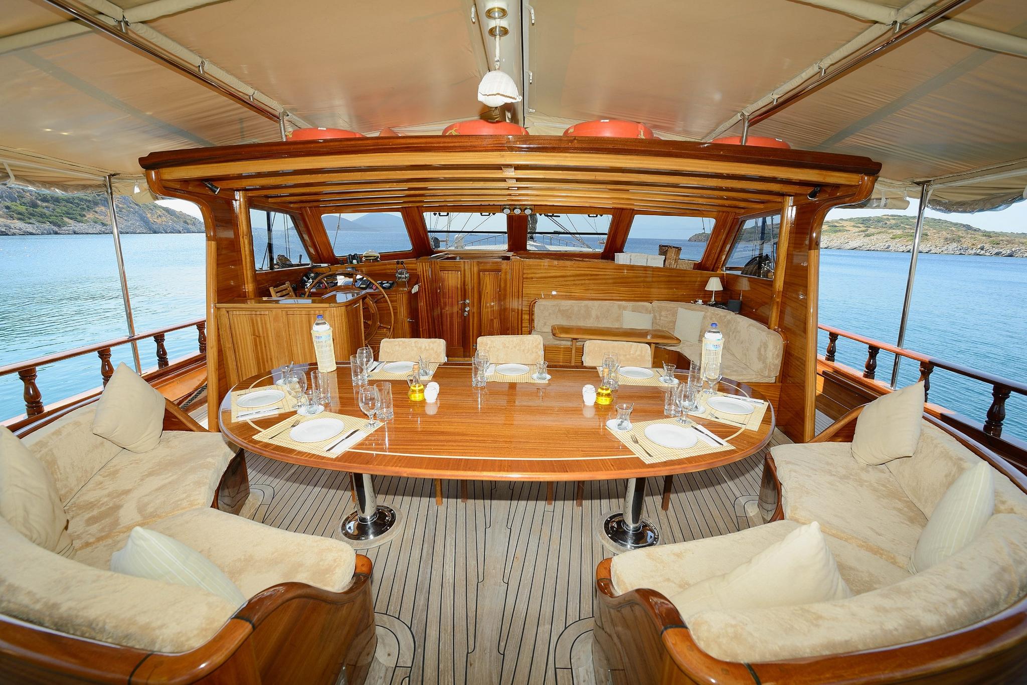 gulet aft deck dining area with oval wooden table and cream cushioned seating under canvas awning