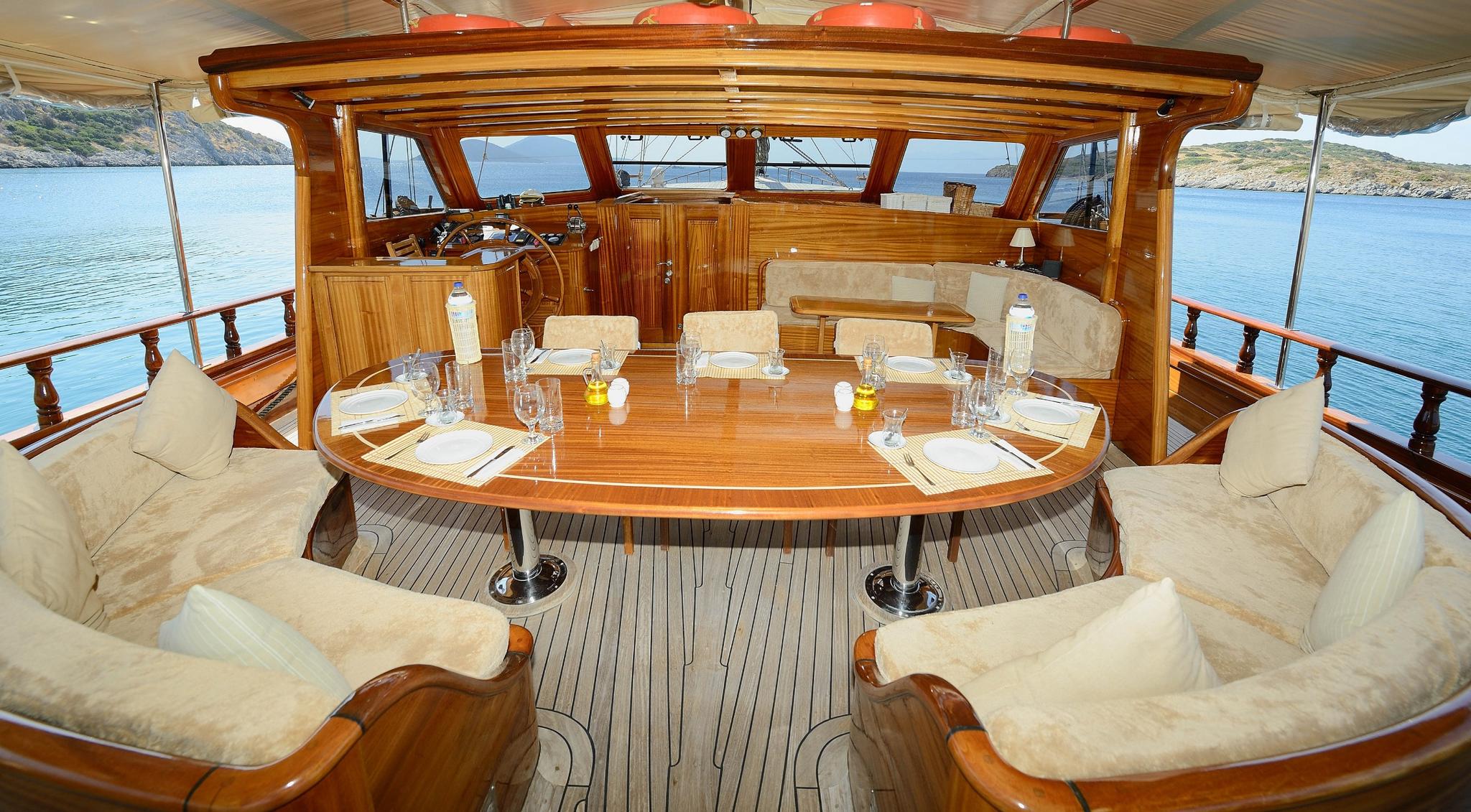 gulet aft deck dining area with oval teak table, cream cushioned seating and coastal views
