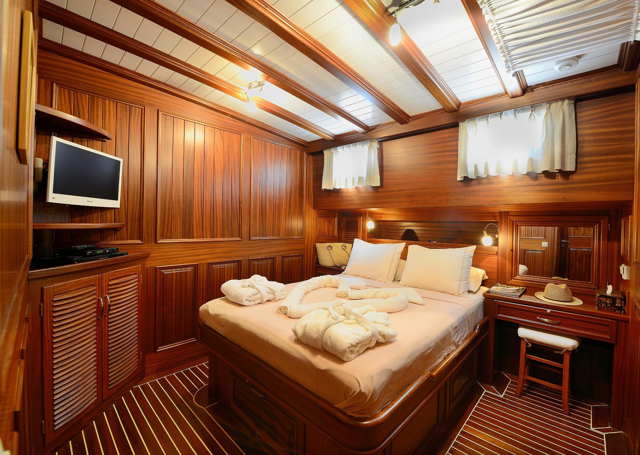 luxury yacht master cabin featuring double bed with white linens, built-in entertainment center with flat screen TV, rich teak wood paneling throughout