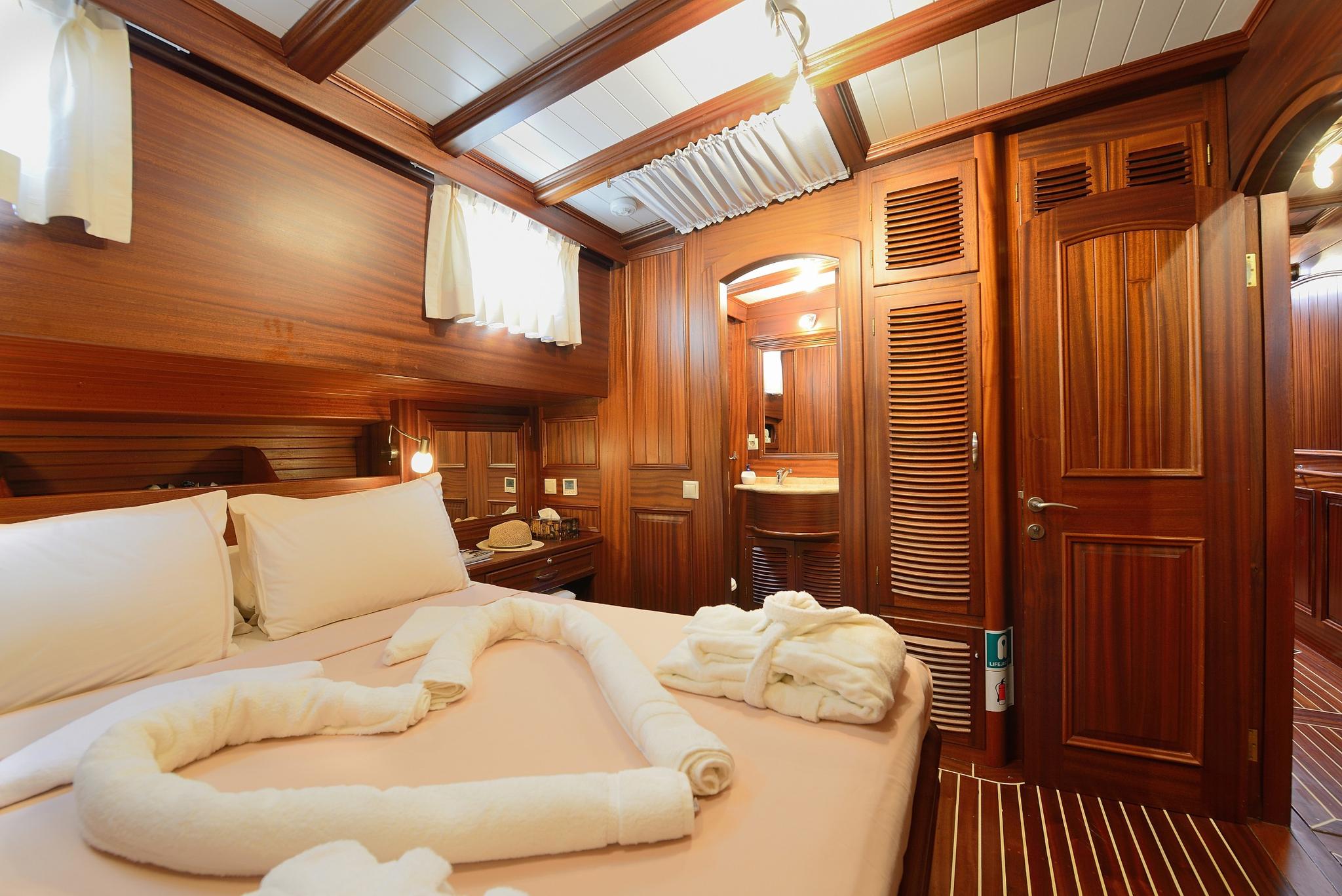 luxury yacht guest cabin featuring double bed with white linens and rich teak wood paneling