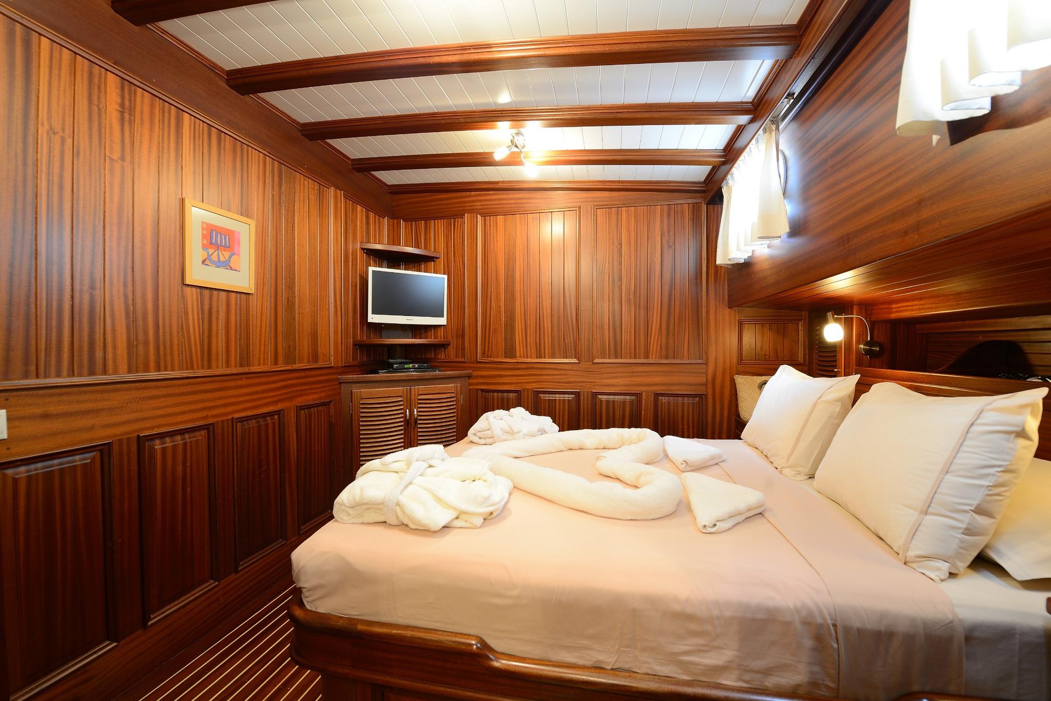 yacht guest cabin featuring double bed with white linens and rich teak wood paneling throughout