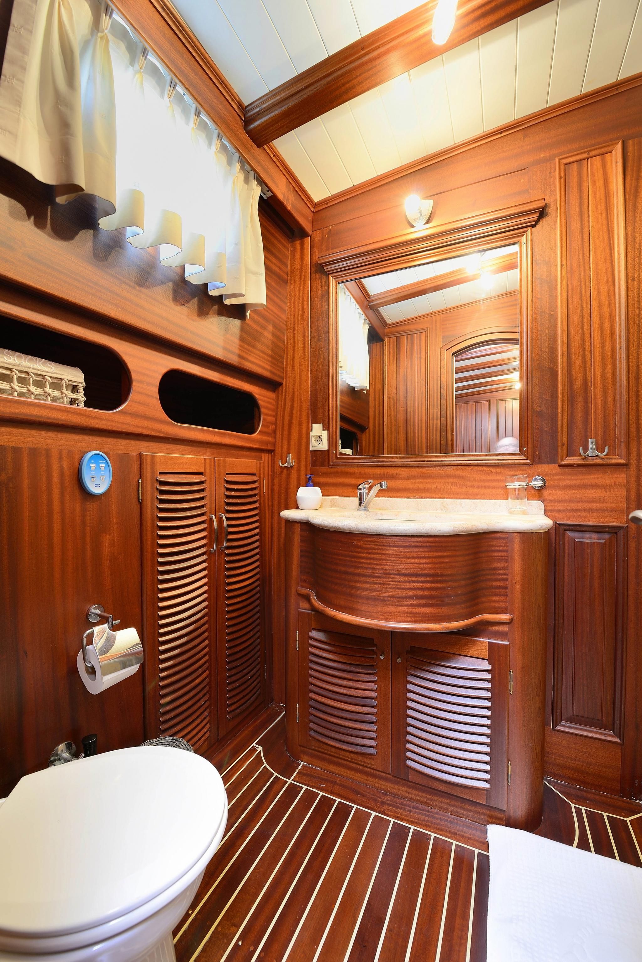 luxury yacht bathroom featuring curved marble vanity, teak cabinetry, skylight and white toilet