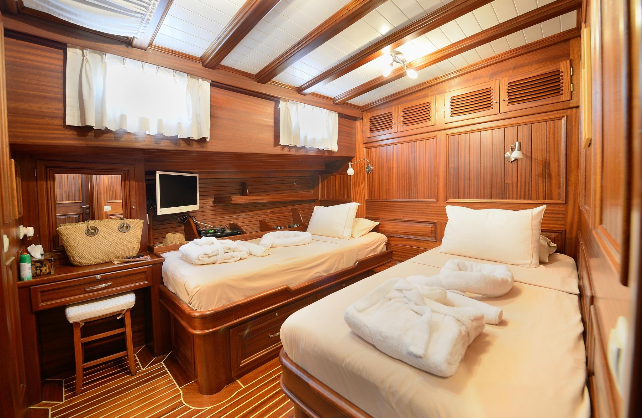 twin guest cabin with two single beds, rich wood paneling, built-in desk and flat screen TV