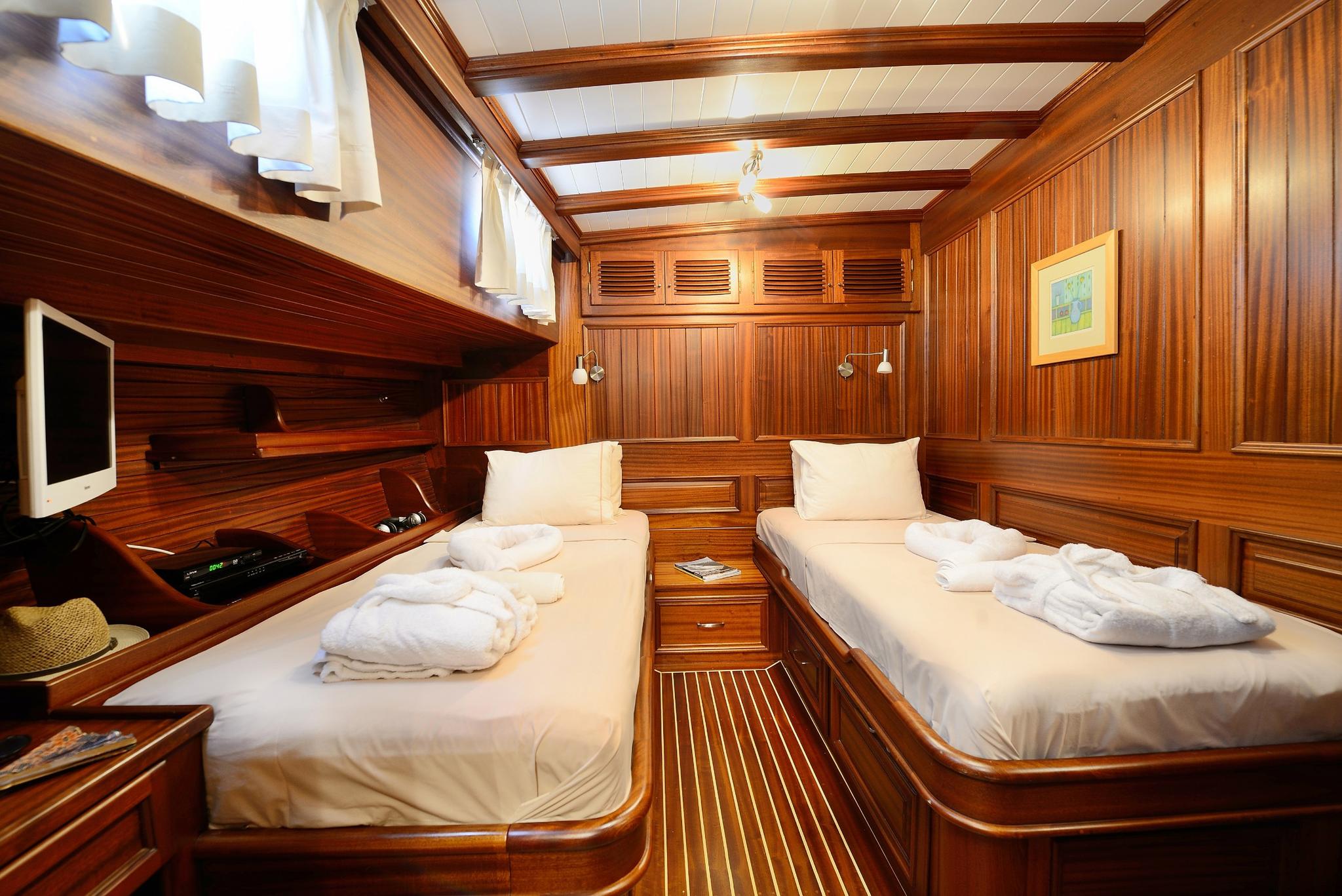luxury yacht twin cabin with two single beds, rich wood paneling and flat screen TV