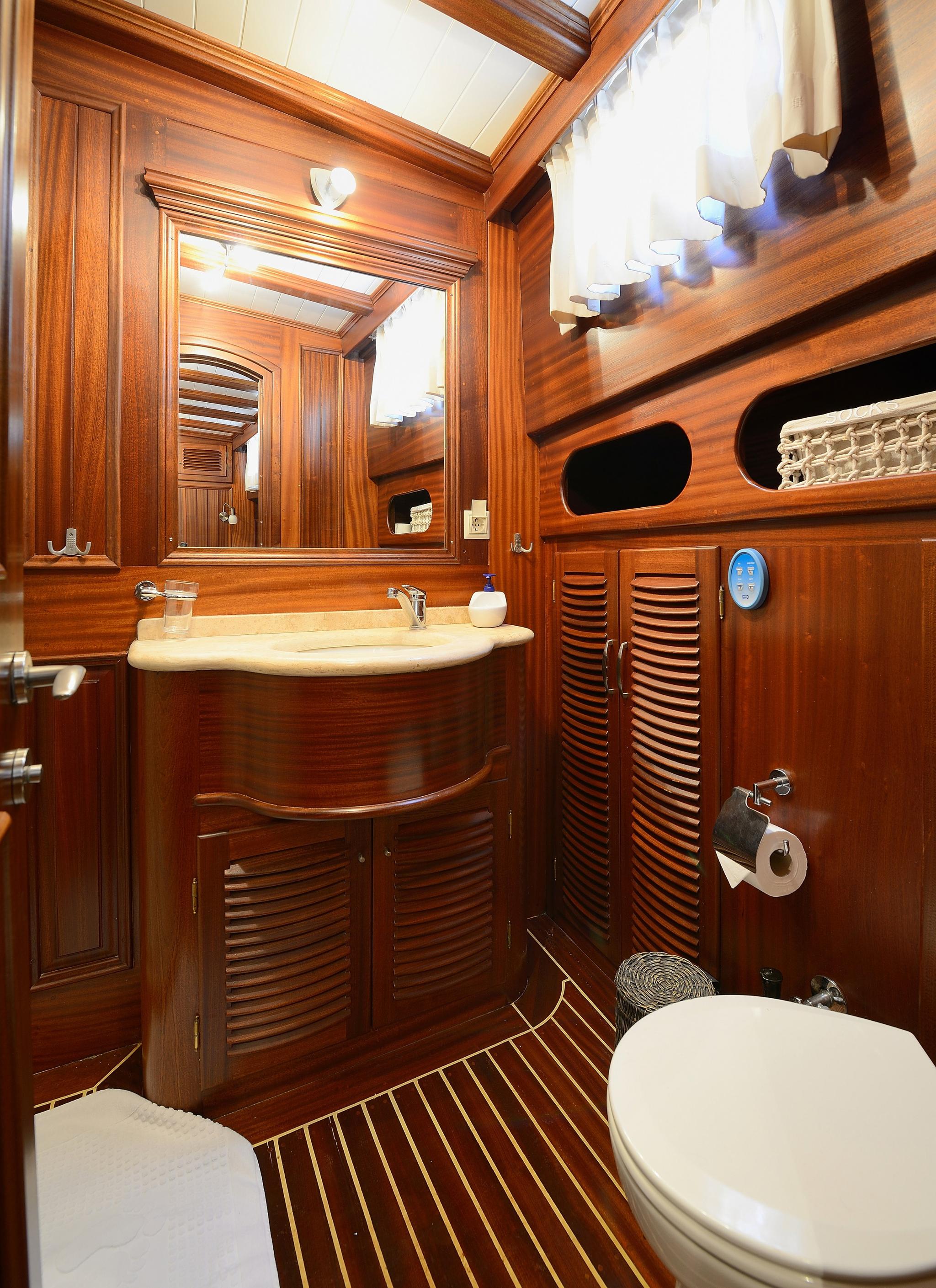 yacht bathroom with teak wood paneling, oval sink, mirror, toilet and skylight
