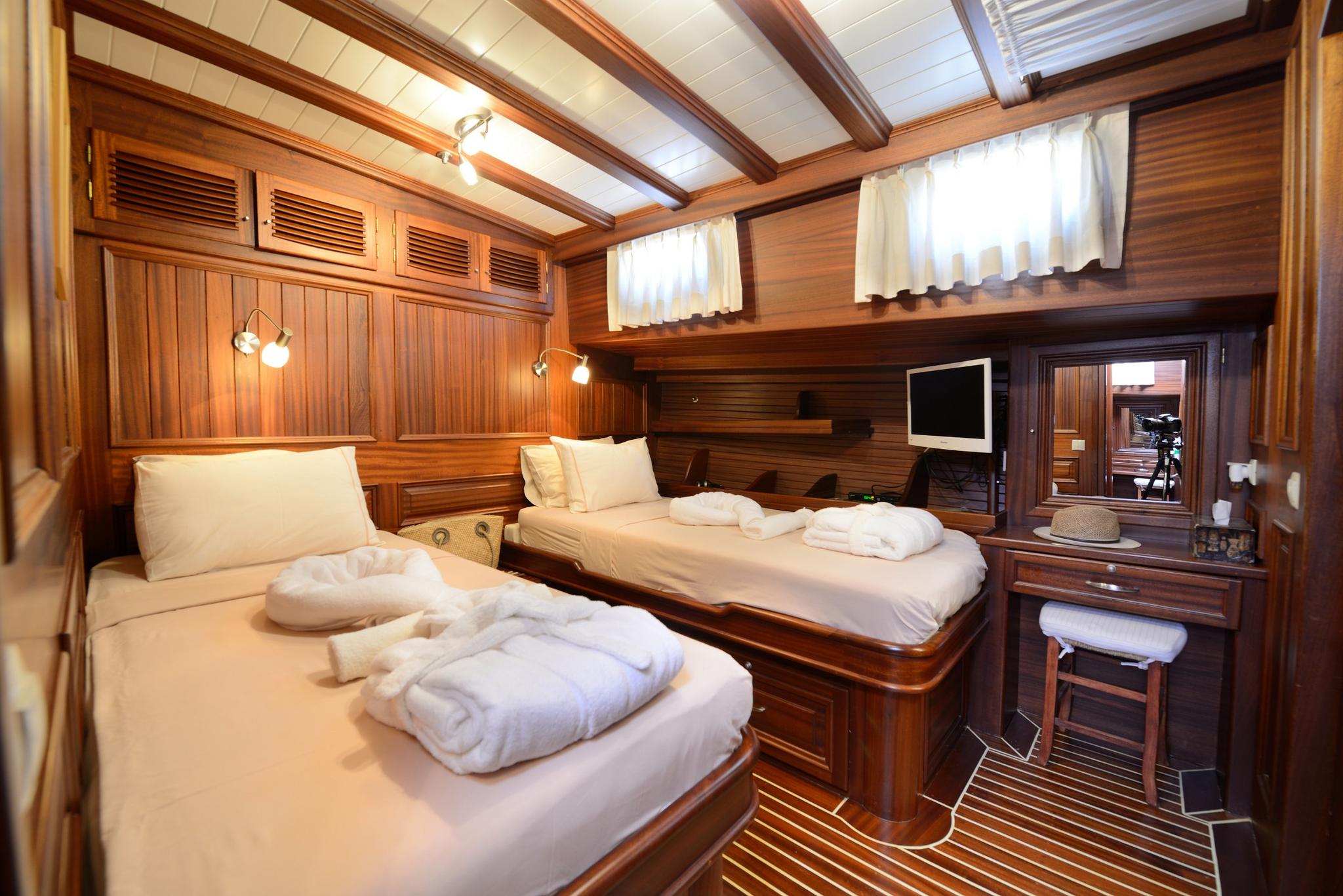 yacht twin cabin with two single beds, rich wood paneling, vanity desk and TV