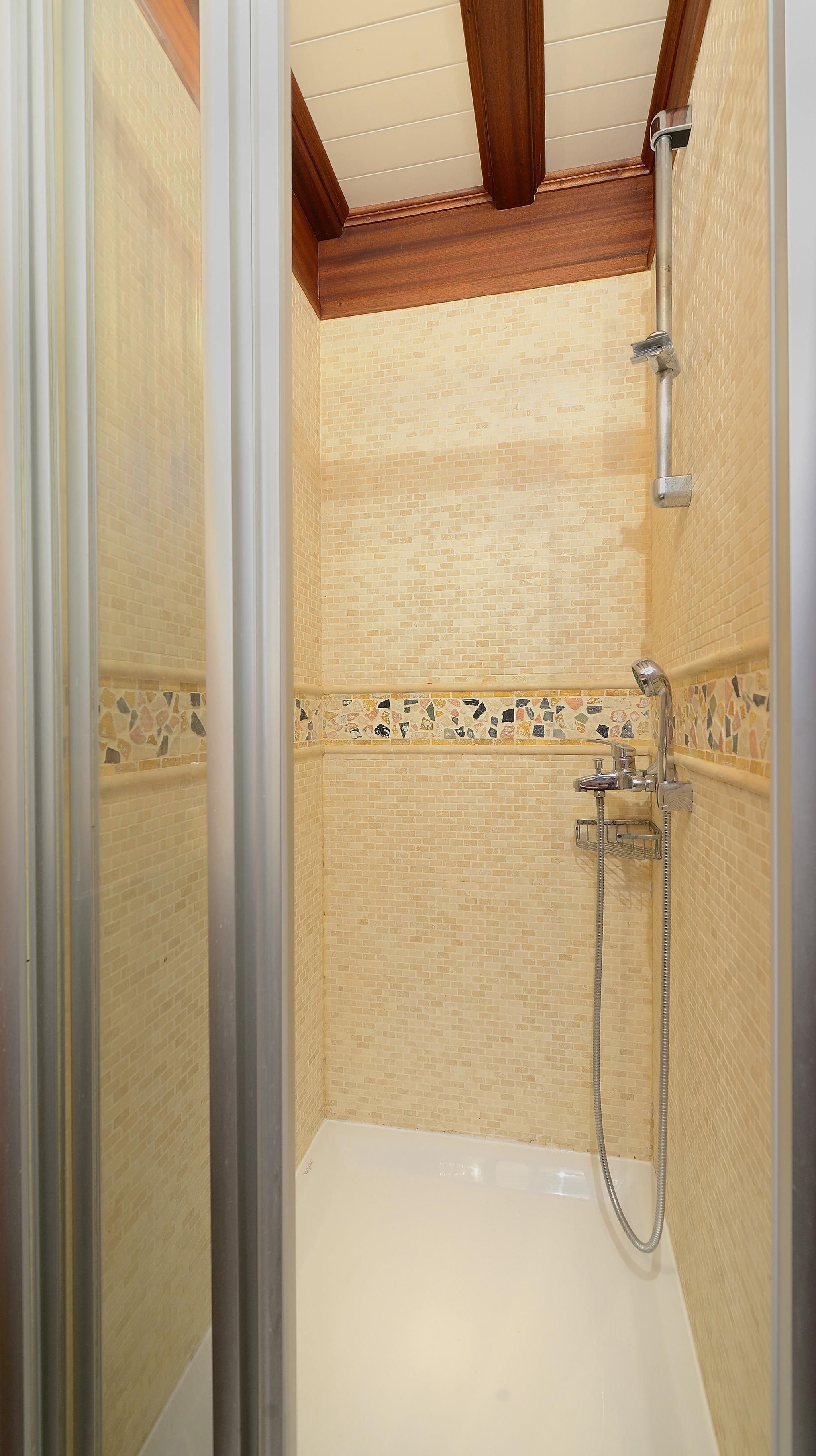 yacht bathroom featuring beige mosaic tiled shower with decorative border and handheld shower fixture