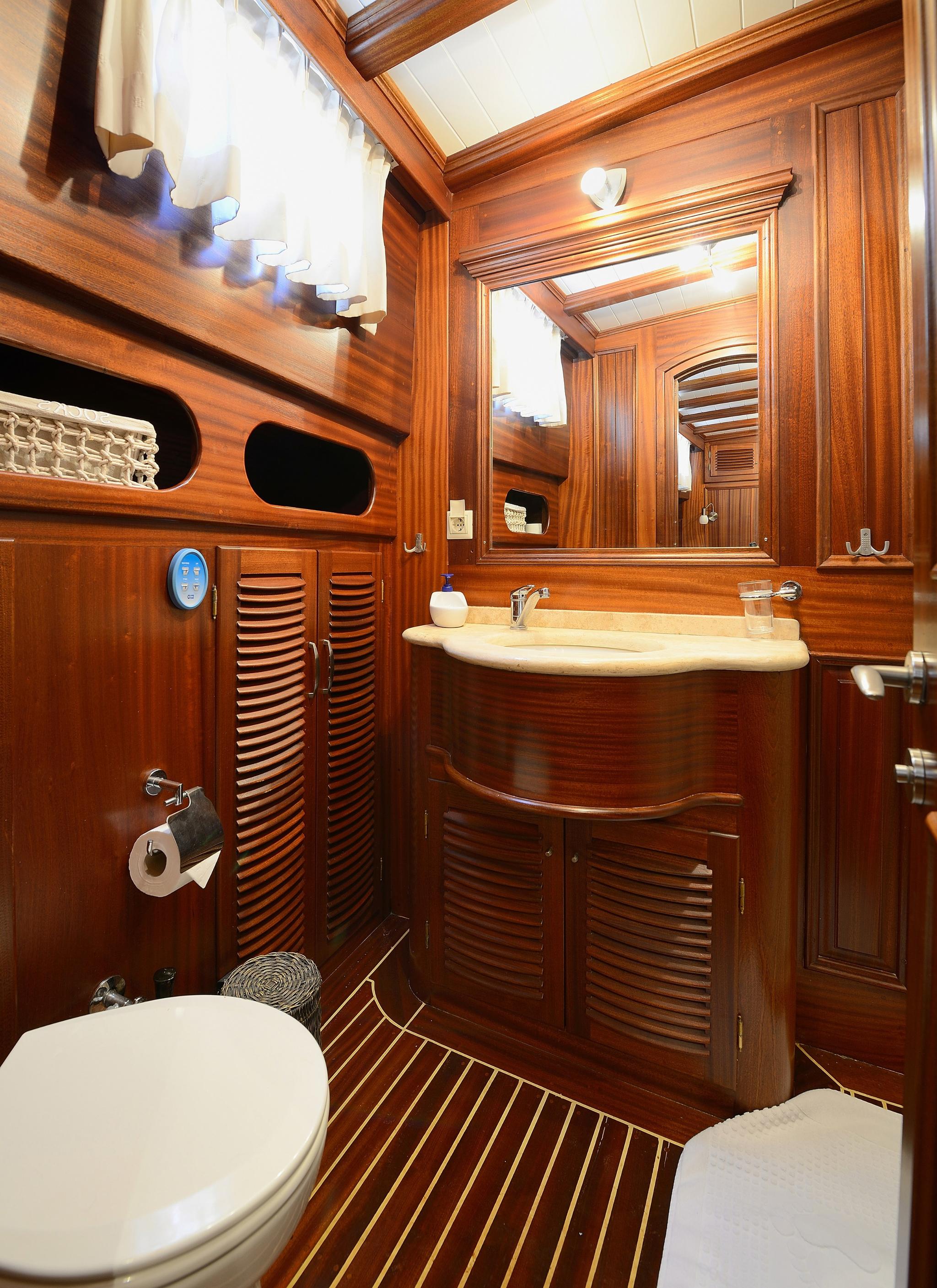 yacht head bathroom featuring rich teak woodwork curved vanity white toilet oval basin