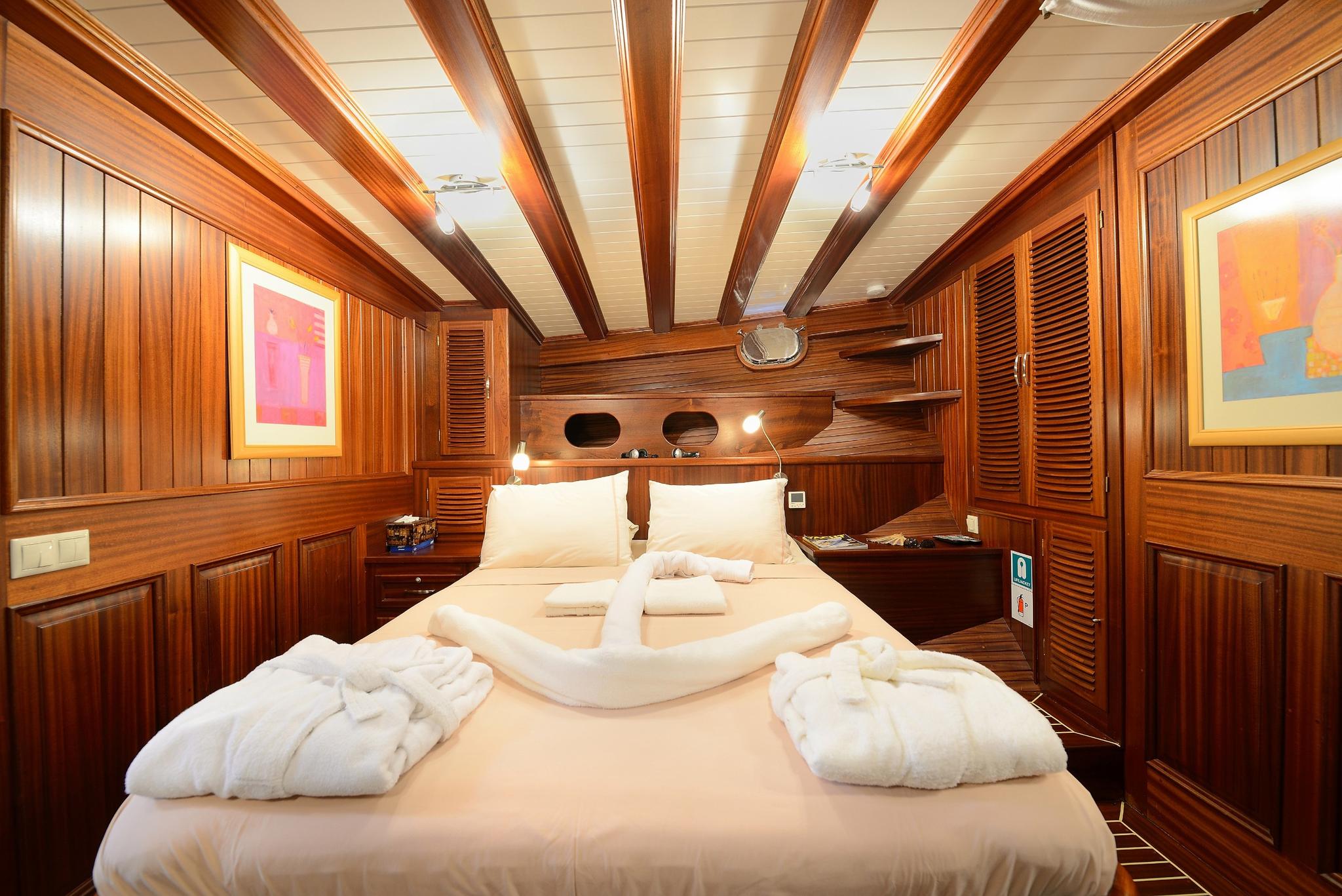 yacht cabin interior with double bed, white linens, exposed wooden beams and paneled walls