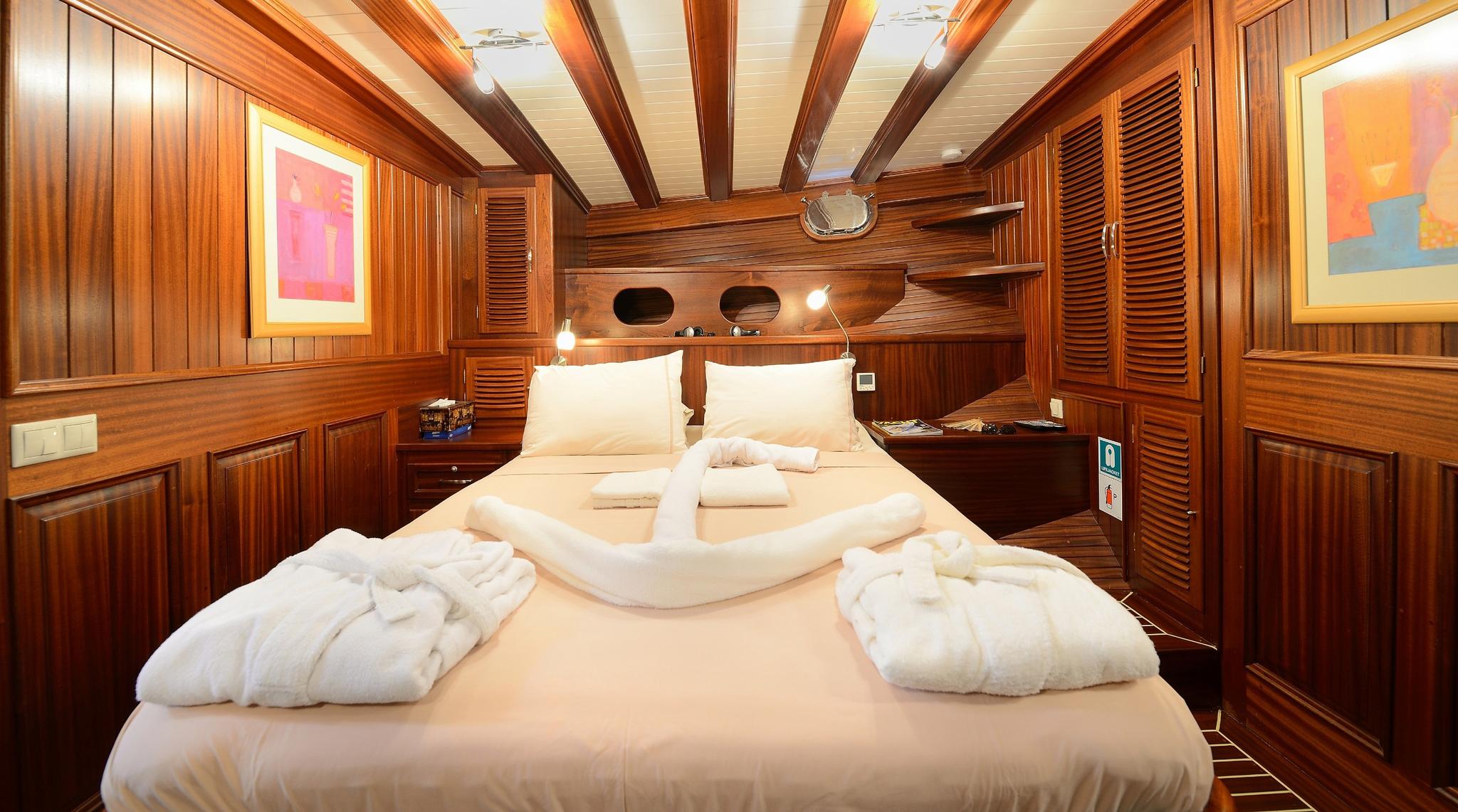 yacht guest cabin featuring double bed with white linens and warm wood interior