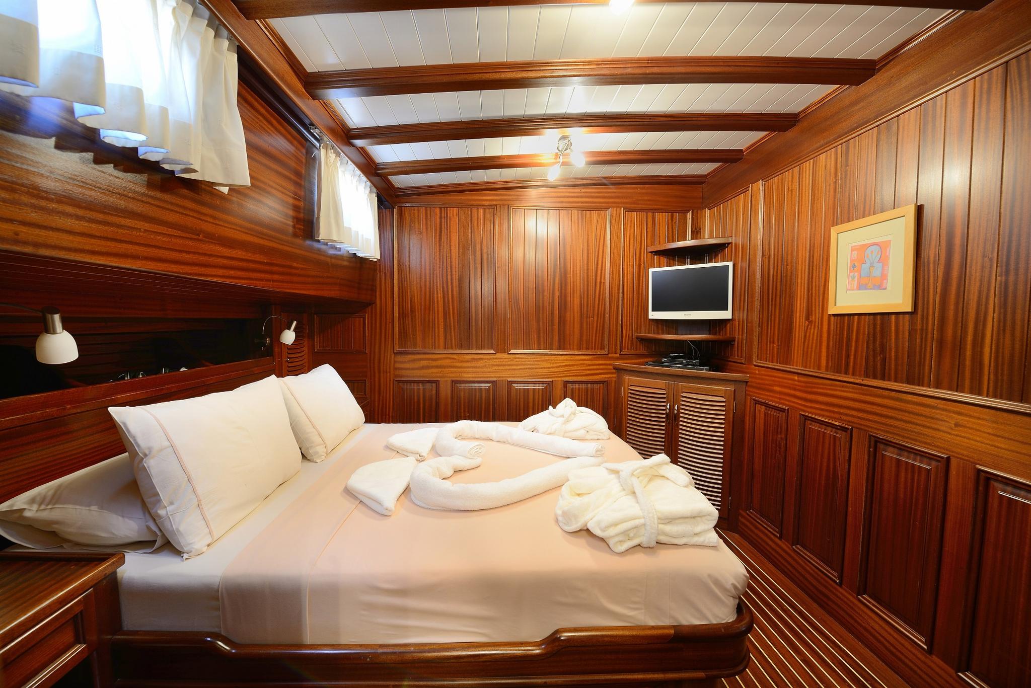 yacht guest cabin featuring double bed, rich teak wood paneling and flat screen TV