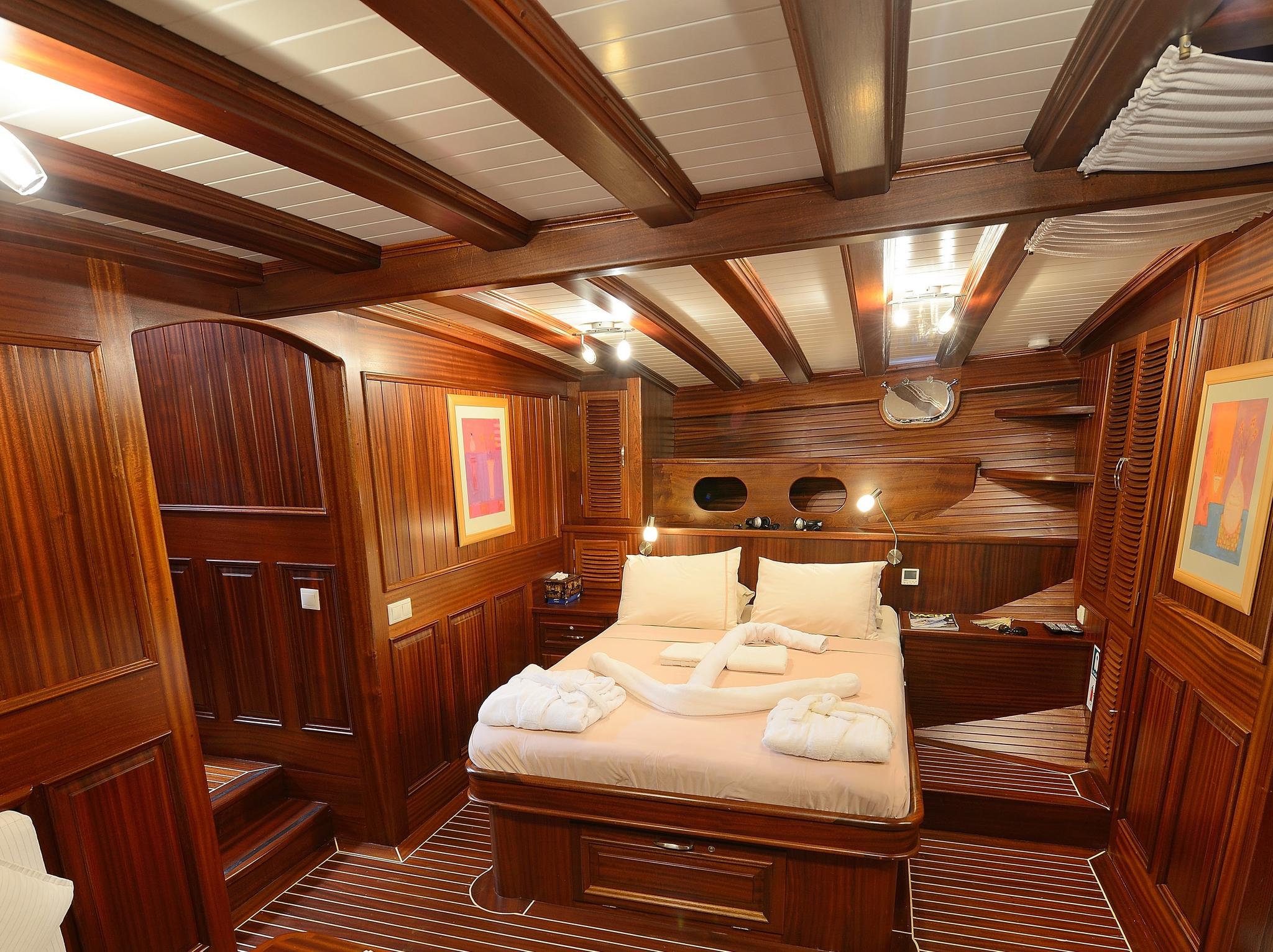 luxury yacht master cabin featuring double bed with white linens and extensive teak wood paneling