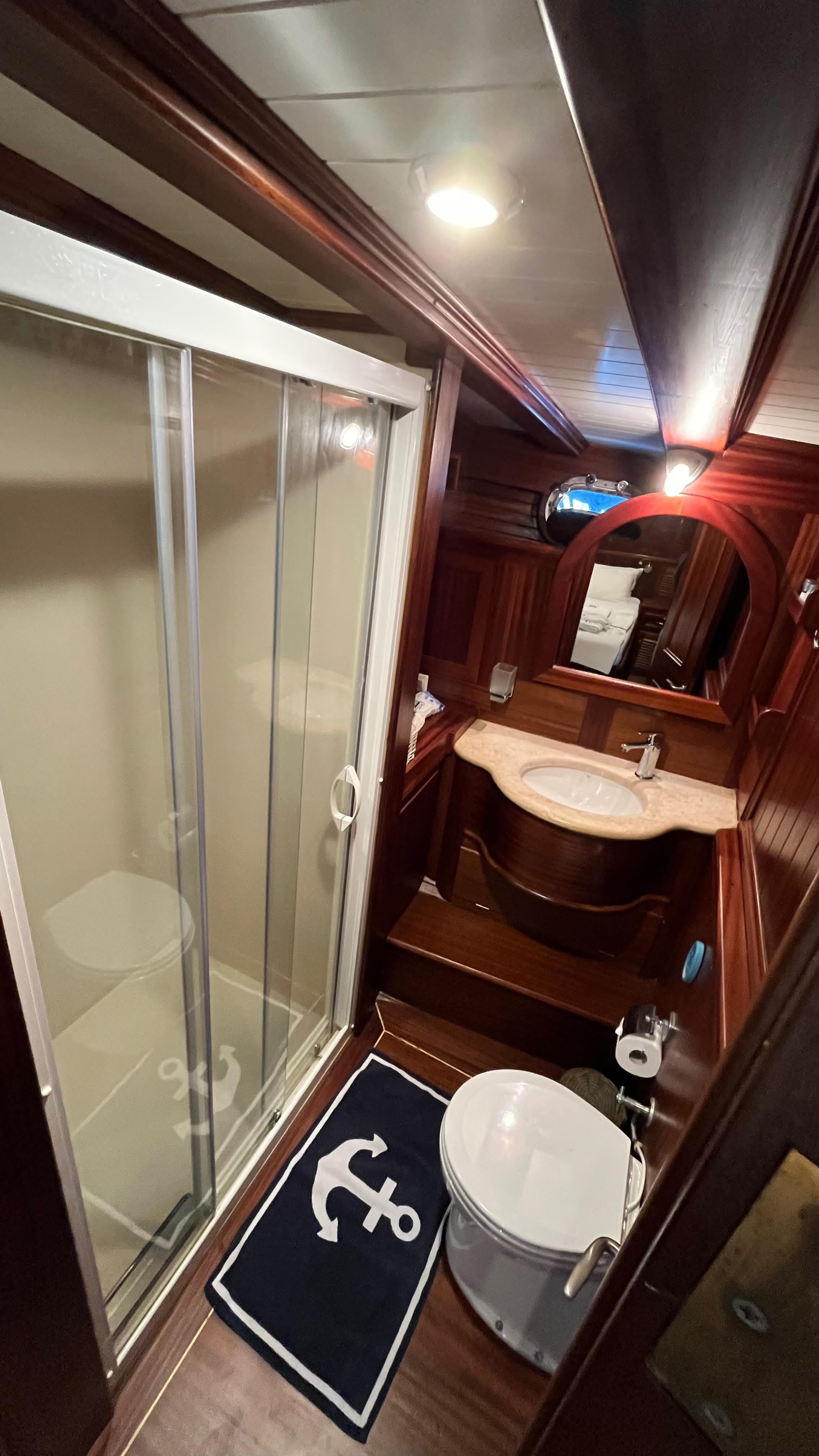yacht en-suite bathroom featuring glass shower enclosure, marble vanity with oval basin, and dark wood finishes