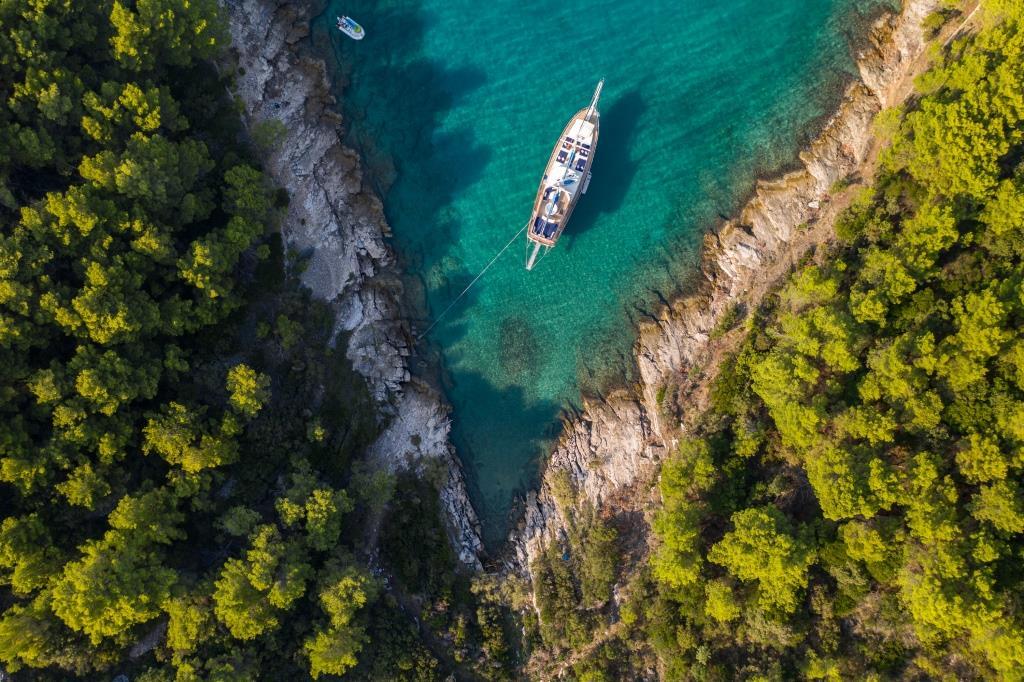aerial view white yacht anchored crystal clear turquoise bay forested coastline