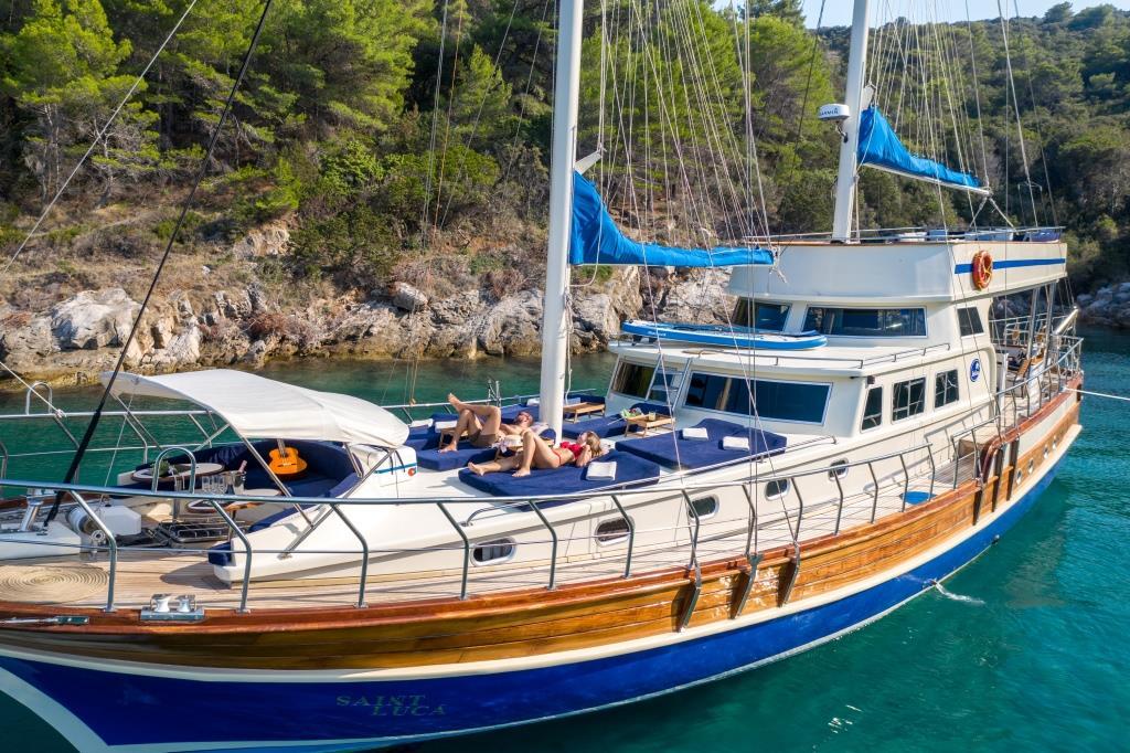 wooden gulet yacht with blue hull anchored in crystal clear Mediterranean bay