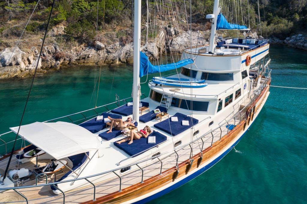 Traditional wooden gulet yacht with guests sunbathing on aft deck in turquoise Mediterranean bay