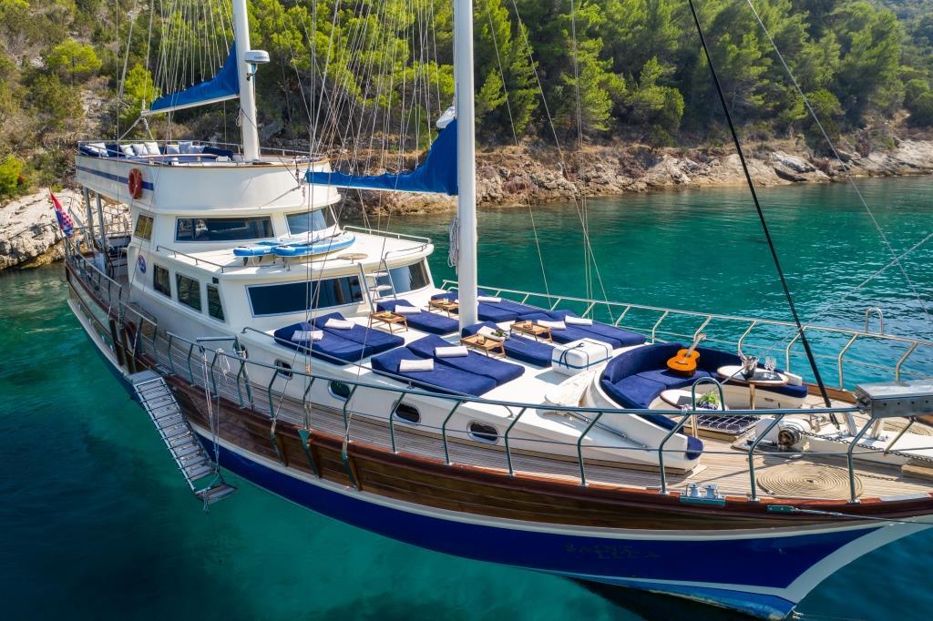 wooden gulet yacht with blue cushions anchored in turquoise Mediterranean bay