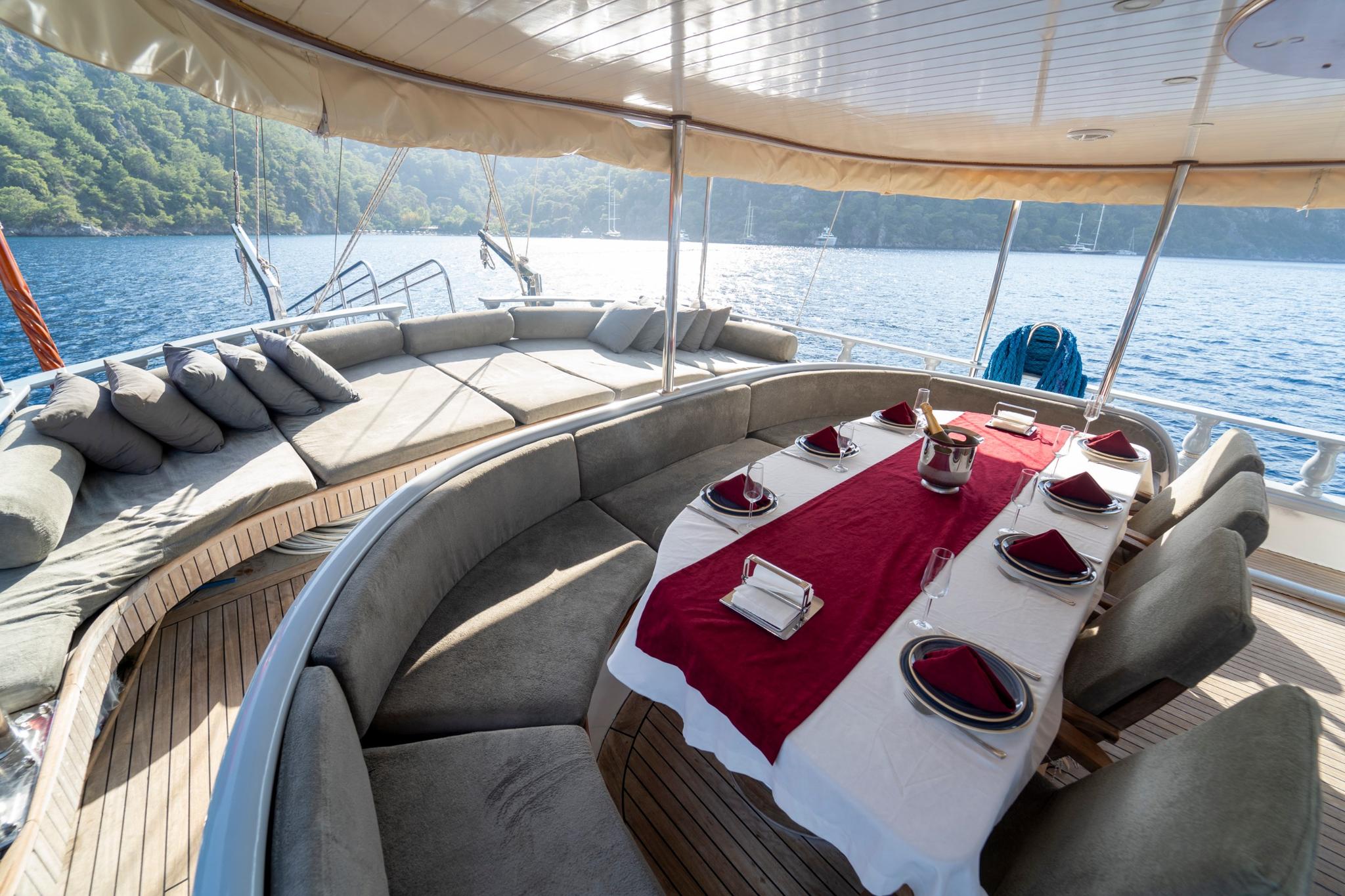 Gulet aft deck with curved seating and formal dining table set with red runner