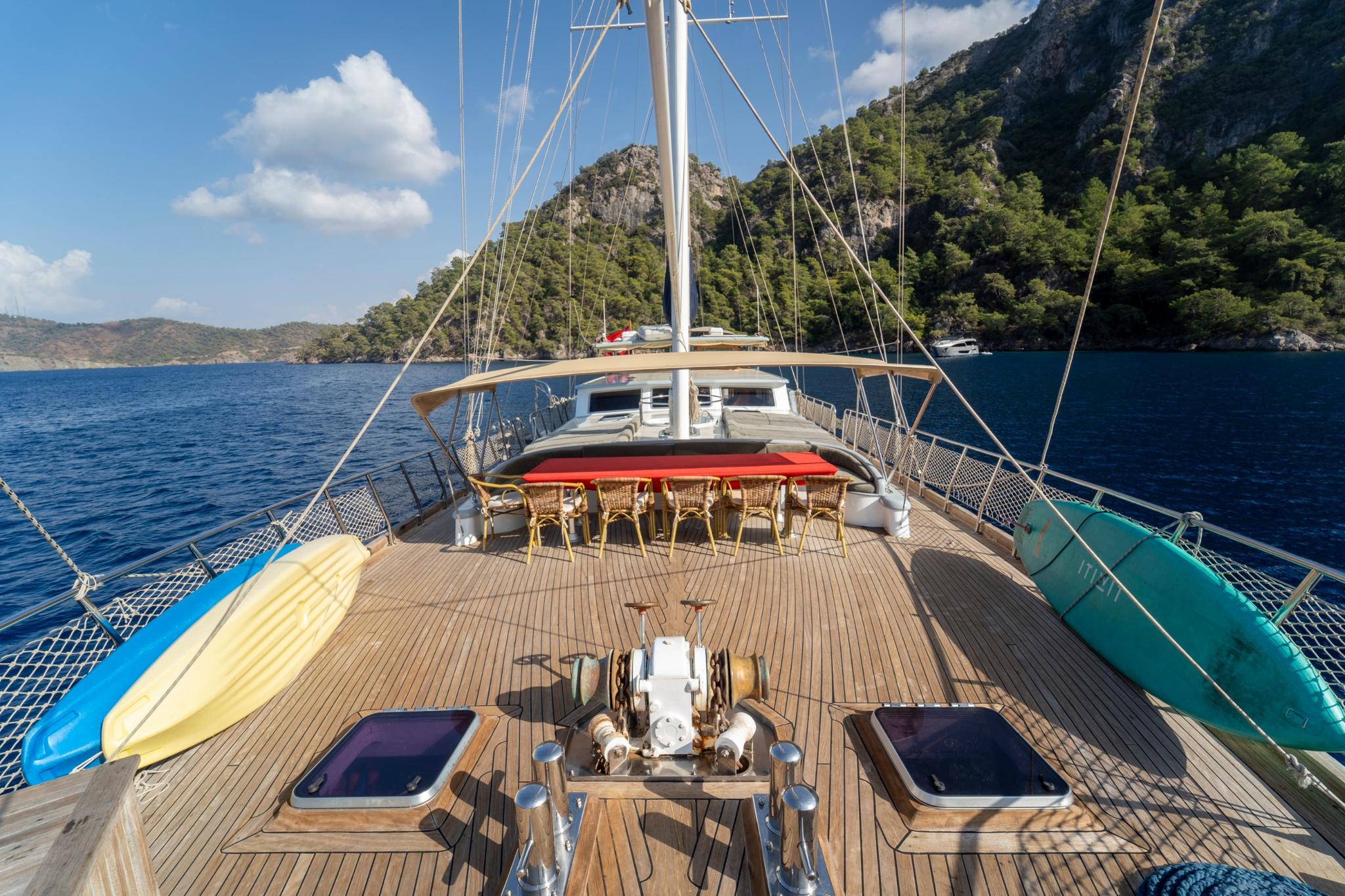 wooden gulet bow deck showing outdoor dining table with wicker chairs and windlass anchor system