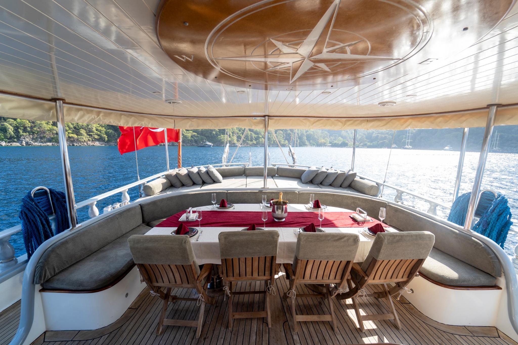 Covered aft deck with curved banquette seating, formal dining table and teak chairs