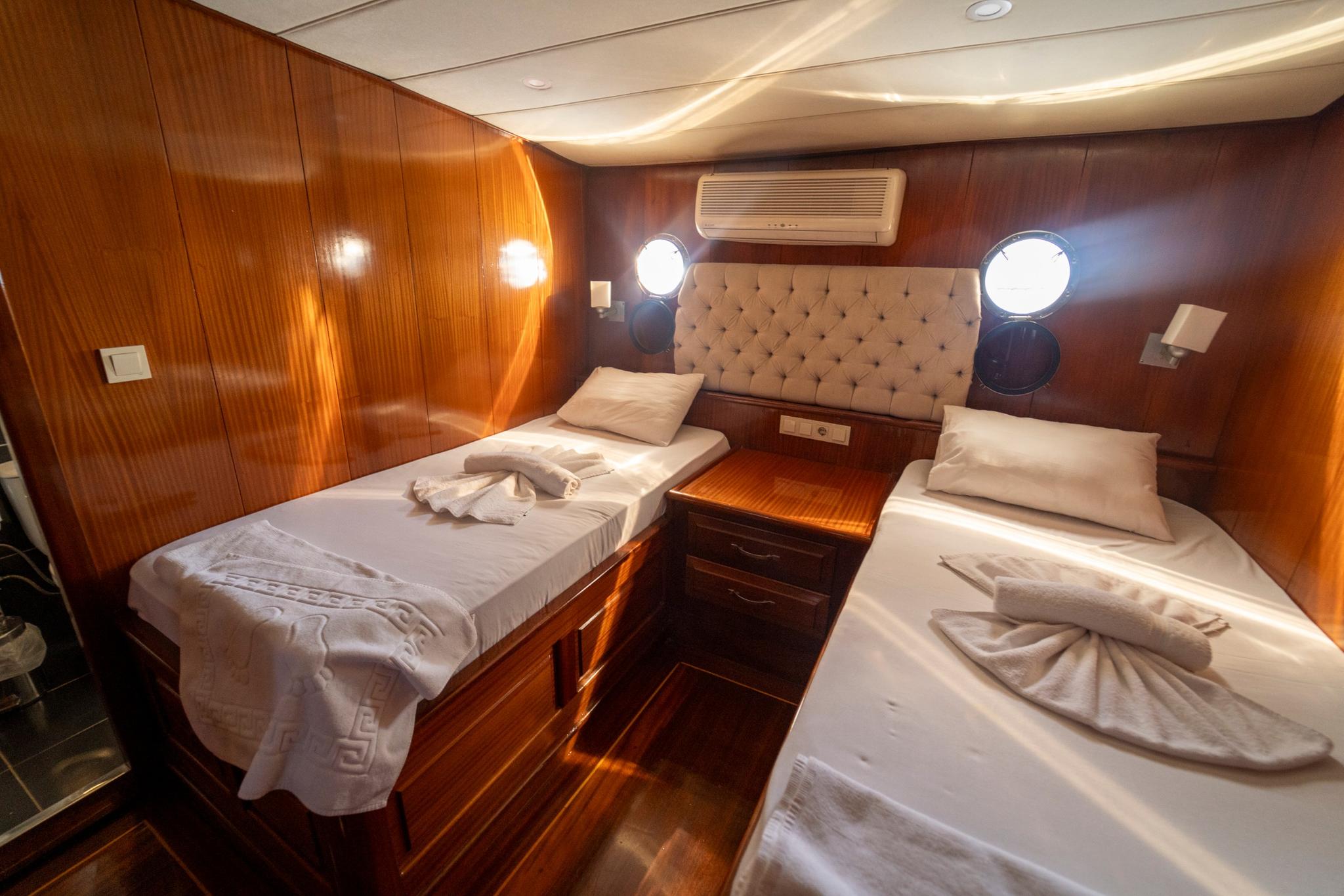 yacht twin cabin with two single beds, tufted headboard, portholes, and wood paneling