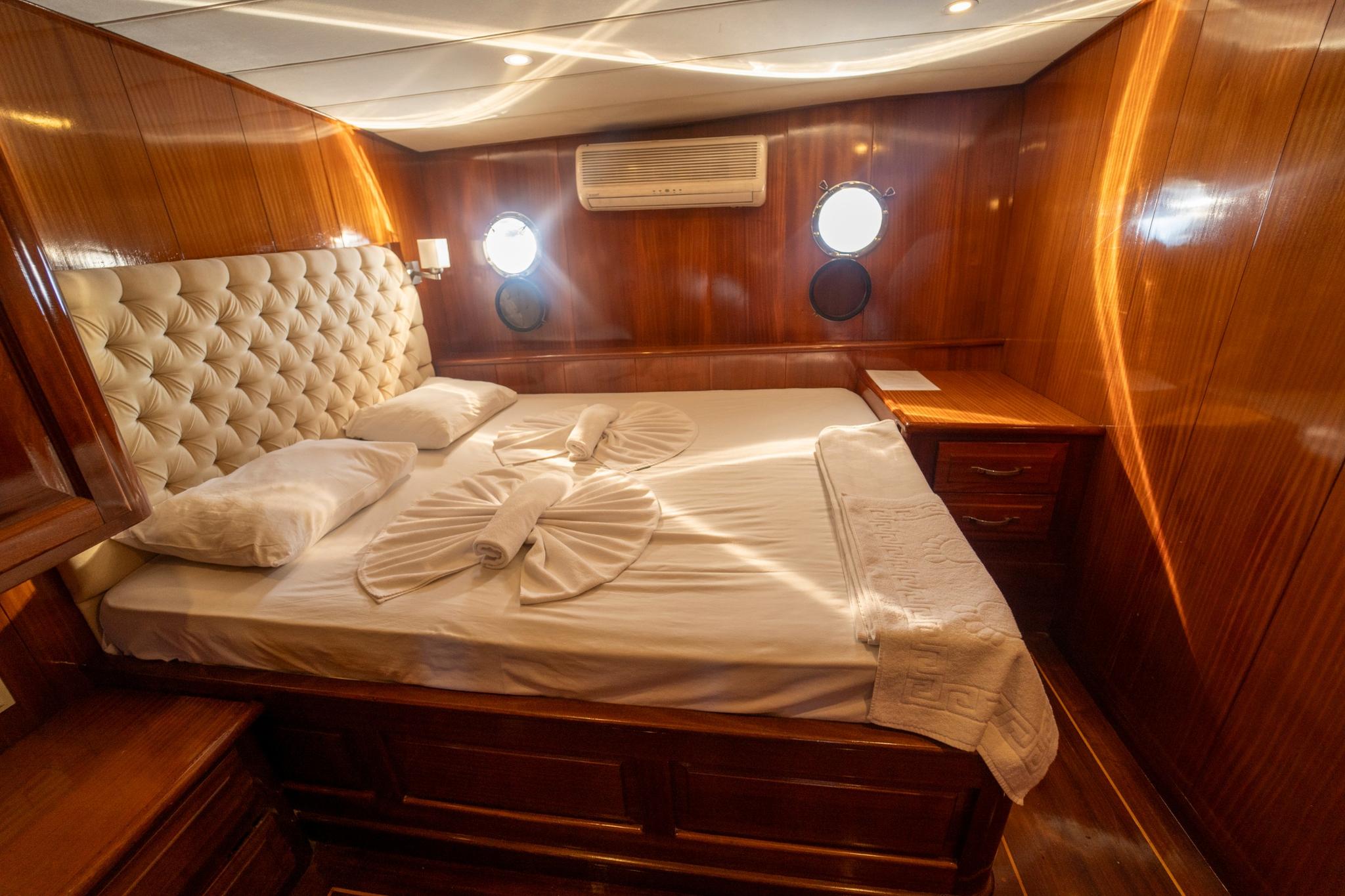 yacht guest cabin featuring double bed with cream tufted headboard and portholes