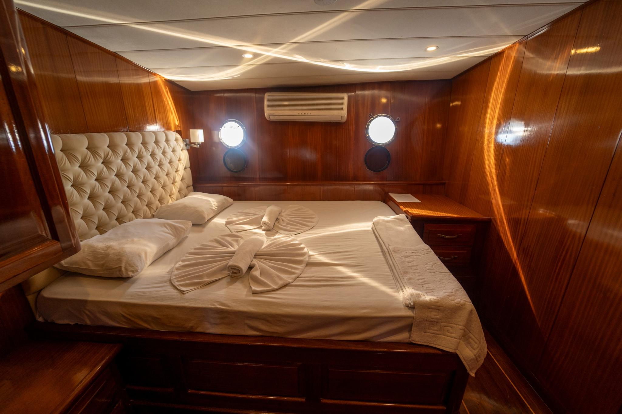 luxury yacht cabin interior featuring double bed with cream tufted headboard and towel arrangement