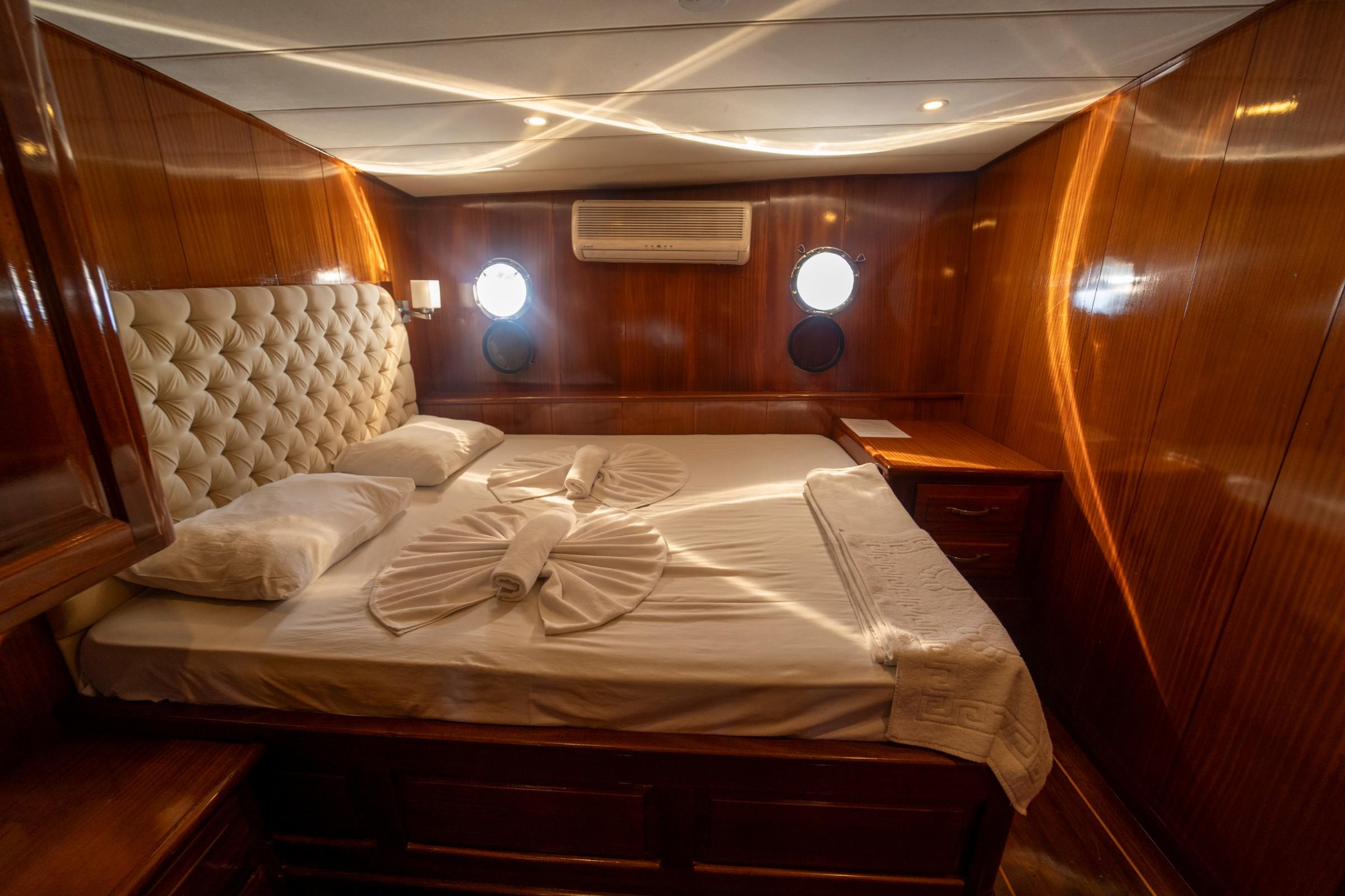 luxury yacht cabin interior featuring double bed with cream tufted headboard and towel arrangement