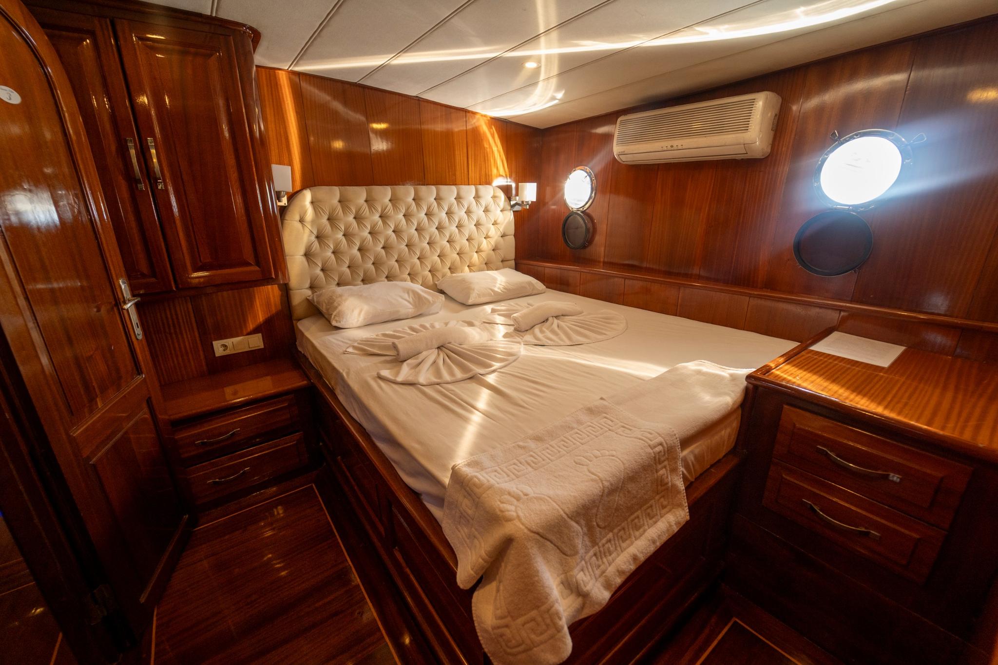 yacht cabin interior with double bed, cream tufted leather headboard, rich wood paneling and portholes