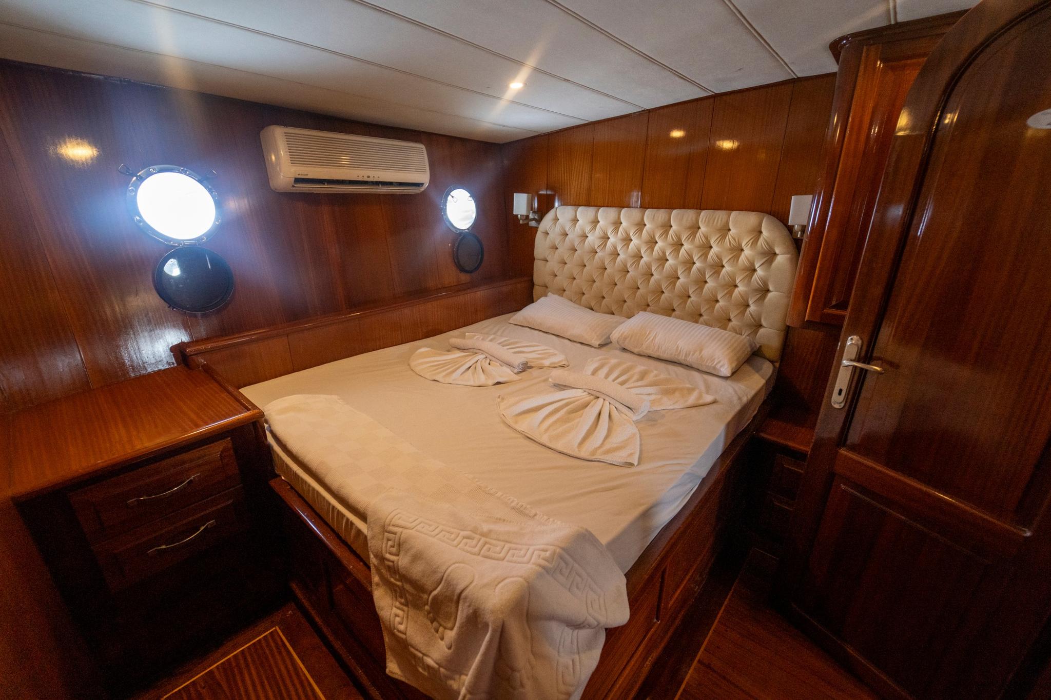 yacht guest cabin featuring double bed with cream tufted headboard and wooden paneling