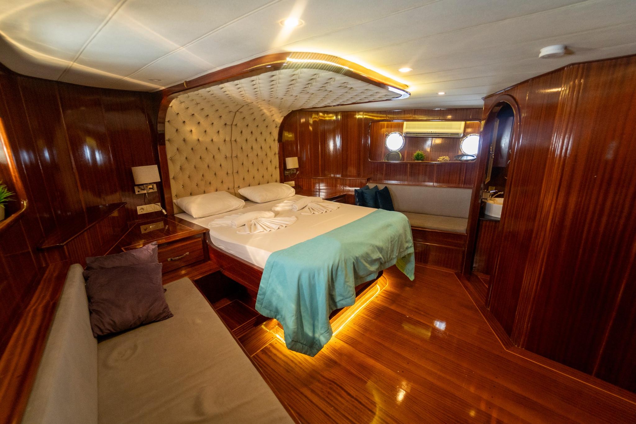 yacht master cabin with double bed, rich wood paneling, upholstered headboard and ambient lighting