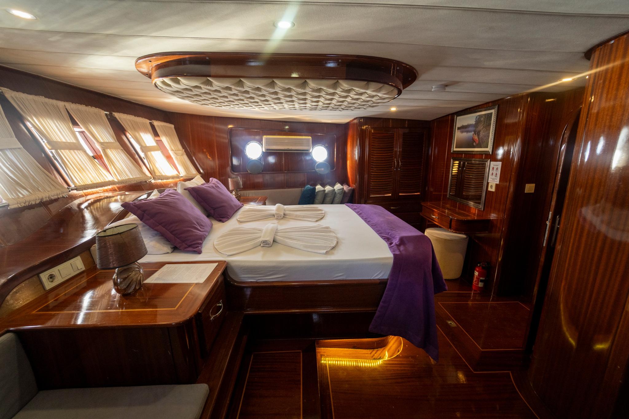 Master cabin featuring king bed with purple linens, ornate ceiling detail, and mahogany woodwork
