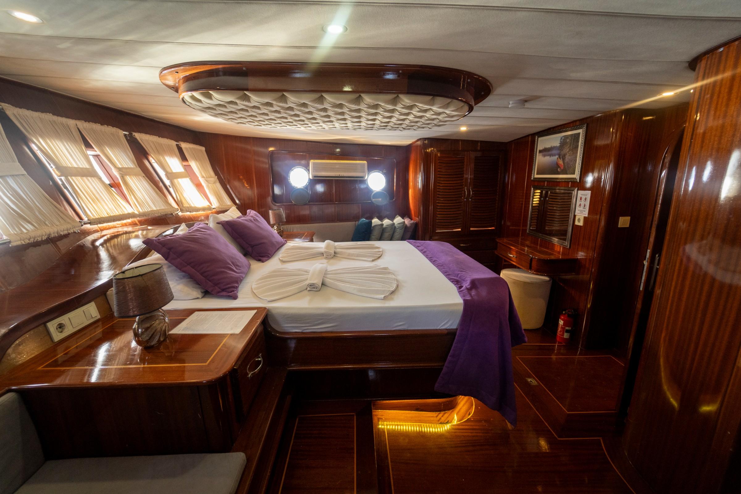 Master cabin featuring king bed with purple linens, ornate ceiling detail, and mahogany woodwork