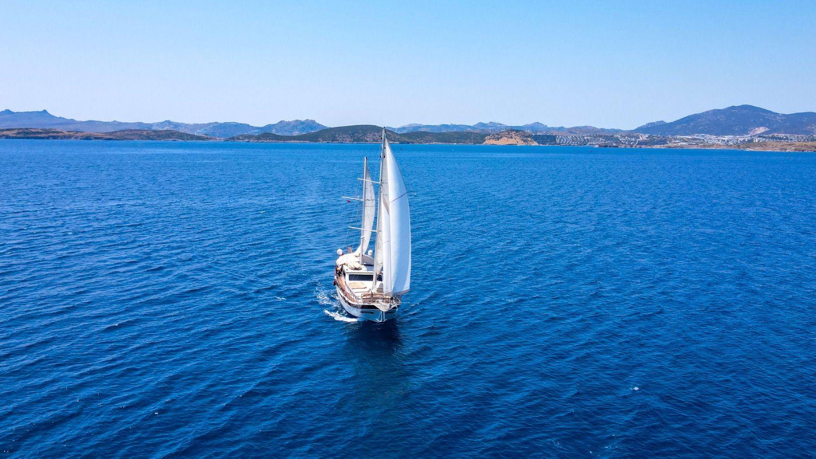 aerial view of white sailing yacht with full sails deployed on deep blue Mediterranean waters
