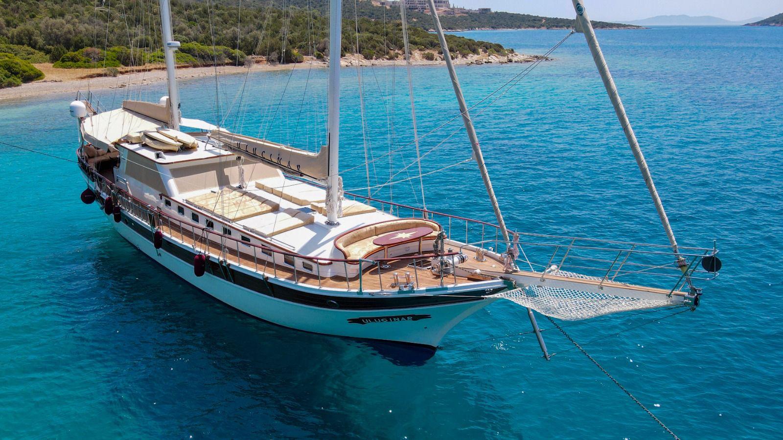 white traditional gulet yacht with two masts anchored in crystal clear turquoise waters near coastline