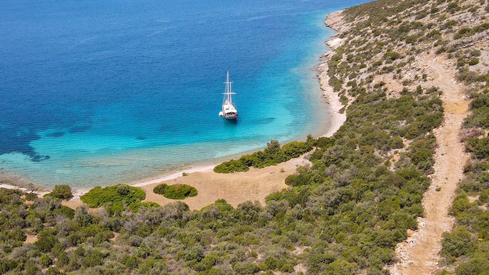aerial view of white sailing yacht anchored in pristine turquoise bay with Mediterranean coastline
