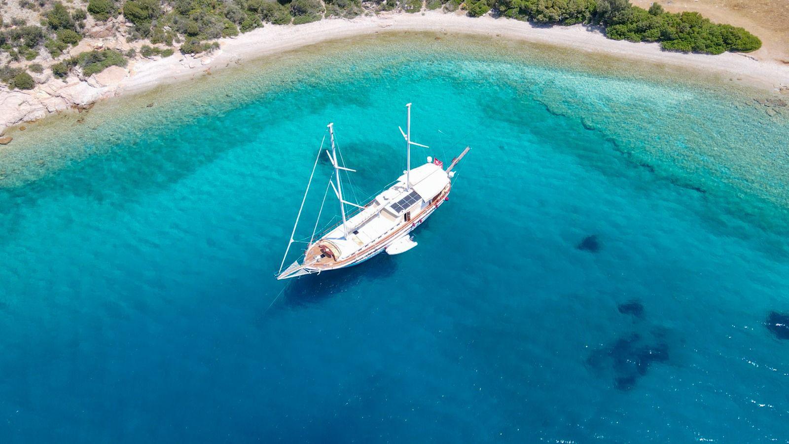 aerial view of white gulet yacht anchored in crystal clear turquoise bay with sandy beach