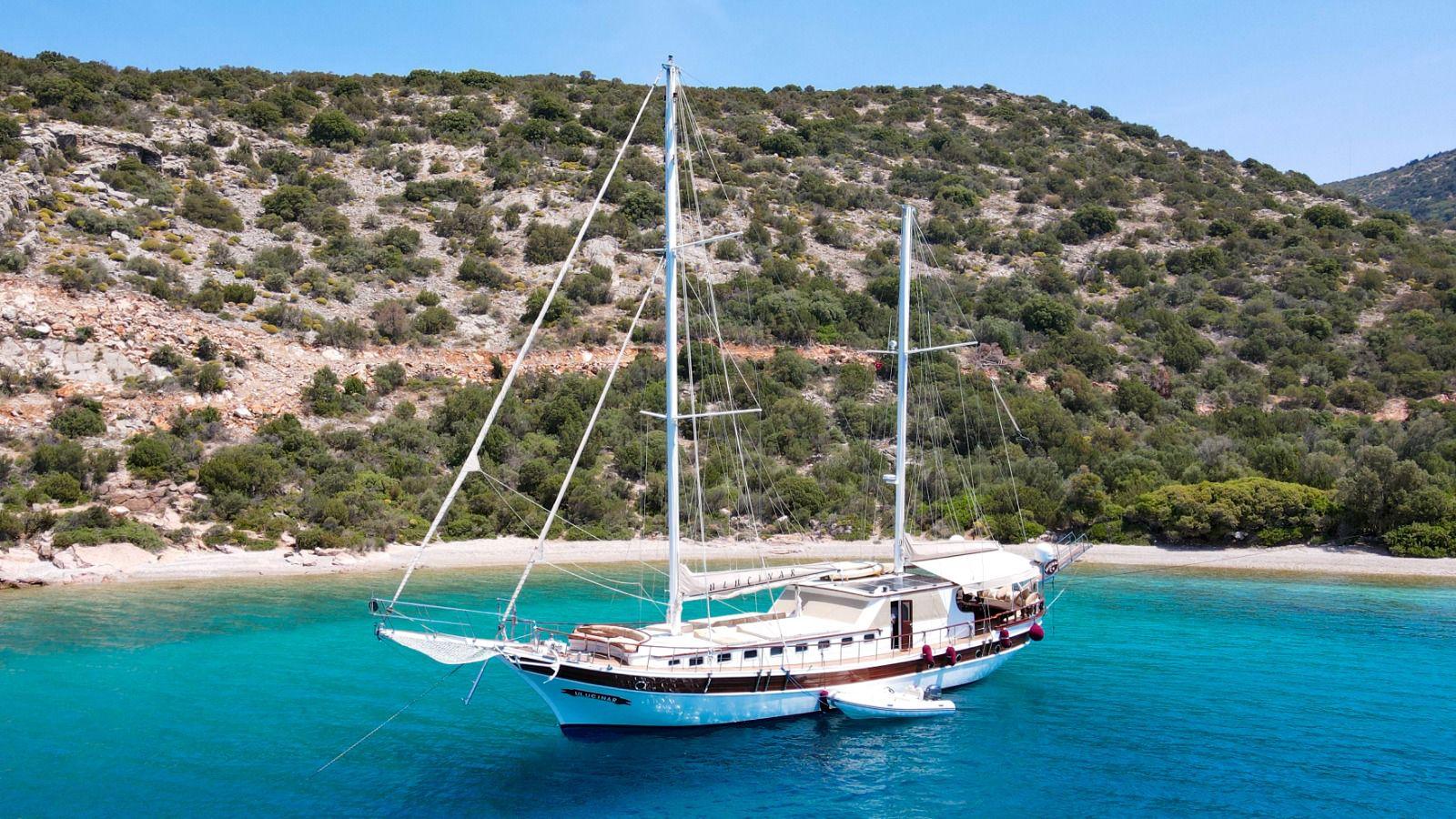 white traditional gulet with two masts anchored in crystal clear turquoise waters near Mediterranean coastline
