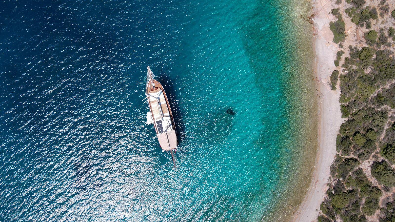 aerial view of white gulet yacht anchored in crystal clear turquoise waters near sandy beach