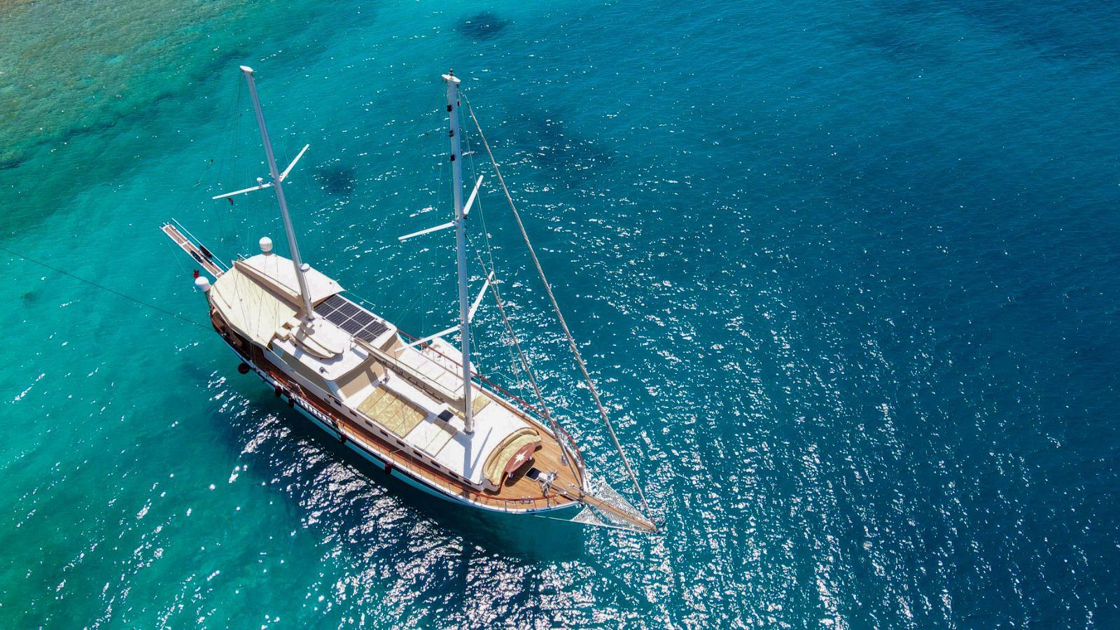 aerial drone shot of traditional wooden gulet yacht with two masts anchored in crystal clear turquoise Mediterranean waters