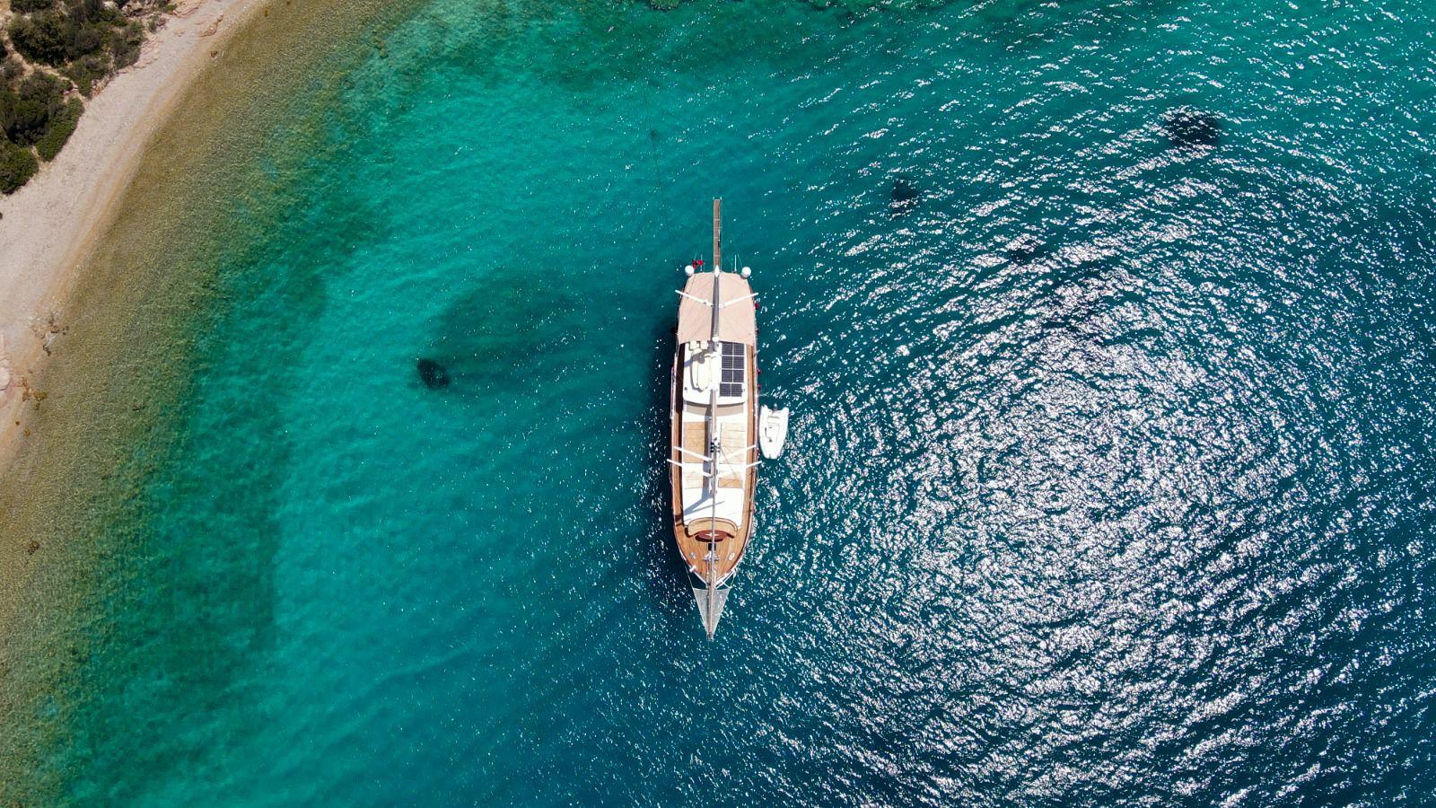 aerial view of traditional gulet yacht anchored in crystal clear turquoise bay near beach