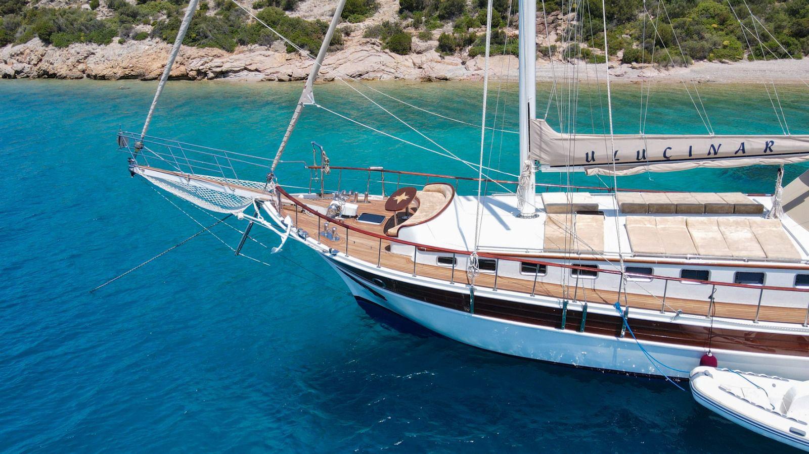 Traditional white gulet yacht anchored in crystal clear turquoise waters near rocky Mediterranean coastline
