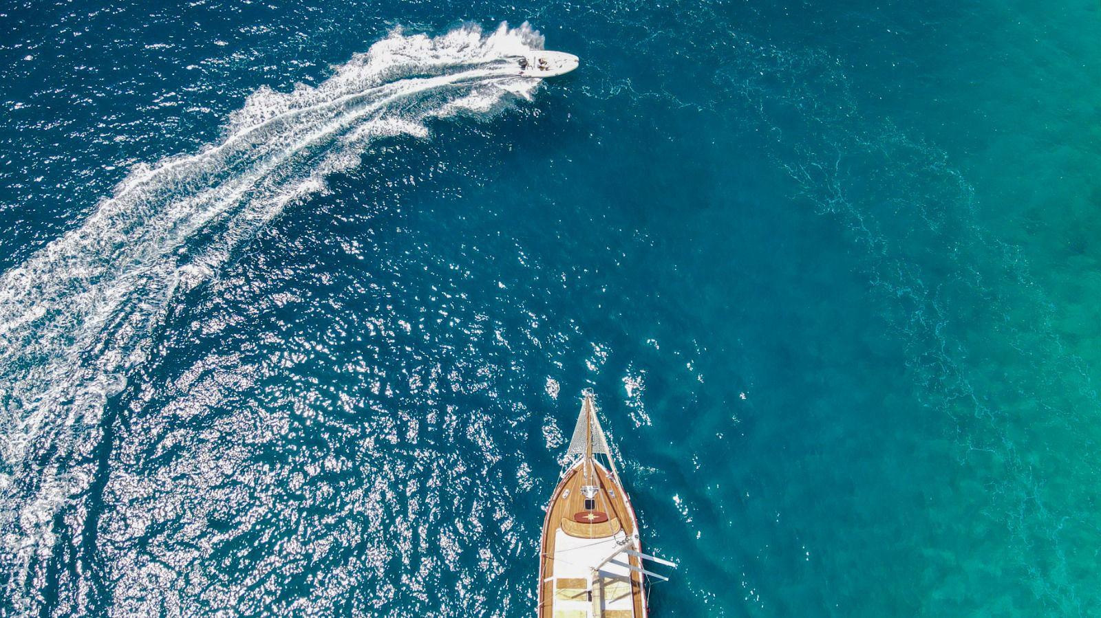 aerial view of luxury yacht creating white wake trail in deep turquoise Mediterranean waters