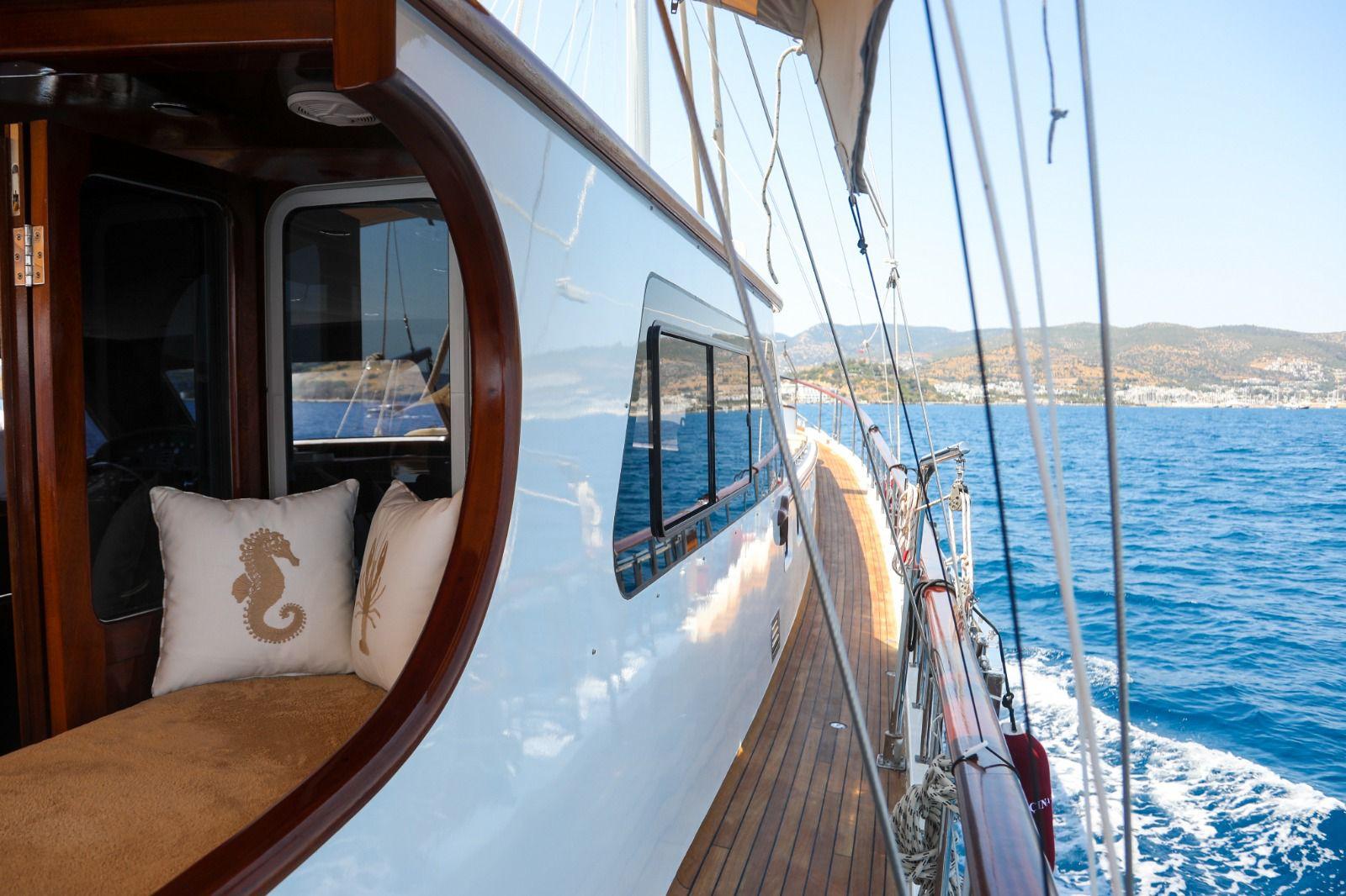 gulet side deck with teak decking, circular porthole window seating area and Mediterranean coastline view