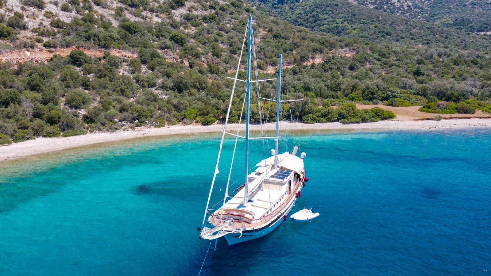 aerial view of white gulet yacht anchored in crystal clear turquoise waters near Mediterranean coastline